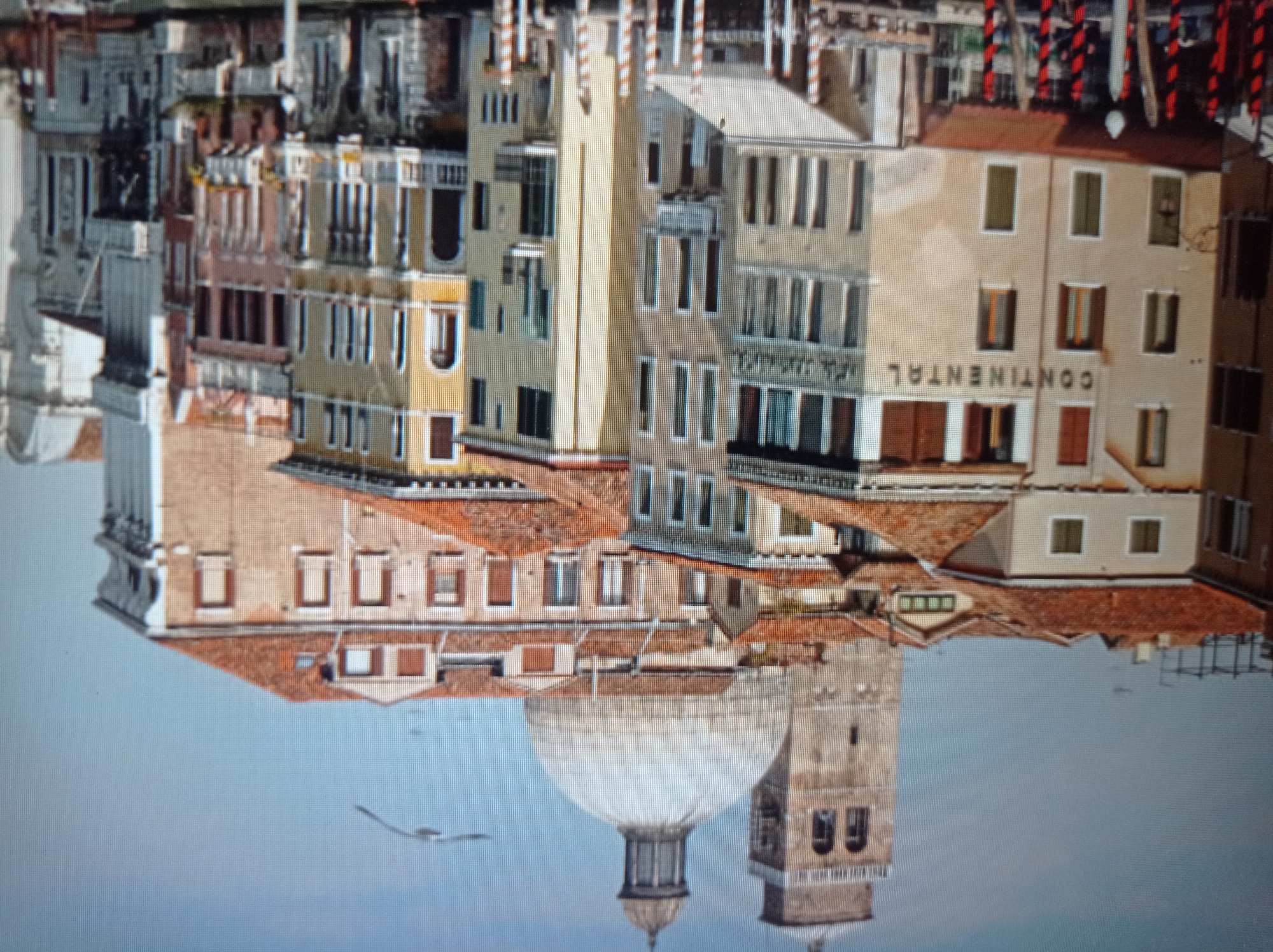 The image depicts a cityscape, likely in Venice, Italy, given the architectural style of the buildings and the presence of canals. Prominent features include a bell tower and a large dome, possibly a cathedral, rising above a cluster of multi-story buildings with terracotta roofs. The buildings are rendered in warm tones, with many windows and balconies. In the foreground, the canal is lined with striped poles. A single bird is visible flying in the pale blue sky. There are no people visible in the image. The scene is a daytime shot, with soft lighting. The crops provided highlight specific architectural details and sections of the cityscape. There is no indication of the city of Mukachevo, Ukraine, in the image or the accompanying crops.