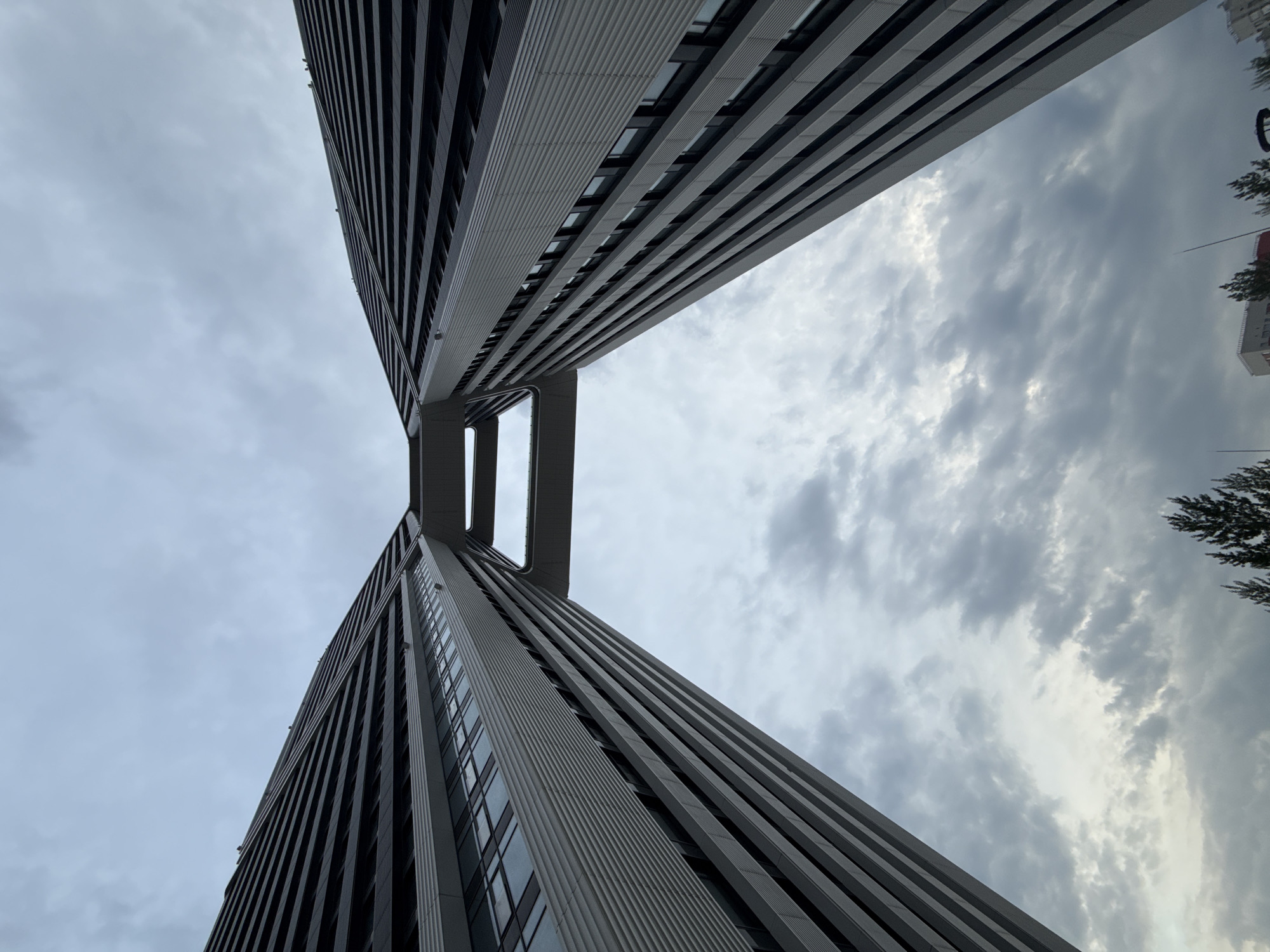 A low-angle shot captures two modern, high-rise buildings in Khimki, Russia, connected by an elevated walkway. The buildings, with their sleek, linear designs, stretch upwards against a cloudy sky. The walkway bridges the gap between the two structures. The buildings' facades consist of repetitive vertical lines and panels. A few trees are visible in the background.
