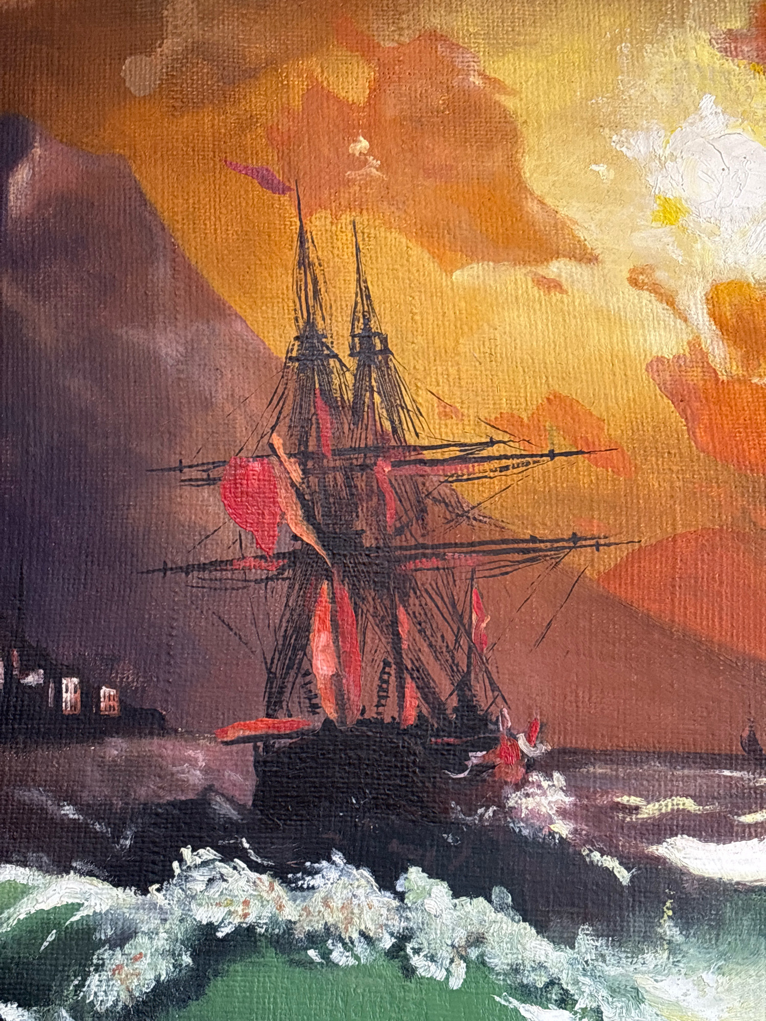 A painting depicts a tall ship with multiple masts sailing through rough, dark seas. The sky is ablaze with a dramatic sunset of oranges, yellows, and pinks, with some white clouds. In the background, silhouetted against the vibrant sky, are dark, imposing mountains. On the left side of the image, there are faint lights suggesting buildings along a shoreline. The ship itself has dark sails, some of which appear to be a deep red, and rigging is clearly visible. The waves are white-capped and turbulent, indicating a stormy condition. The painting's style is expressive, with visible brushstrokes that give texture to the canvas. There are no people visible in the scene. This image does not depict any location in the city of Ijevan, Armenia.