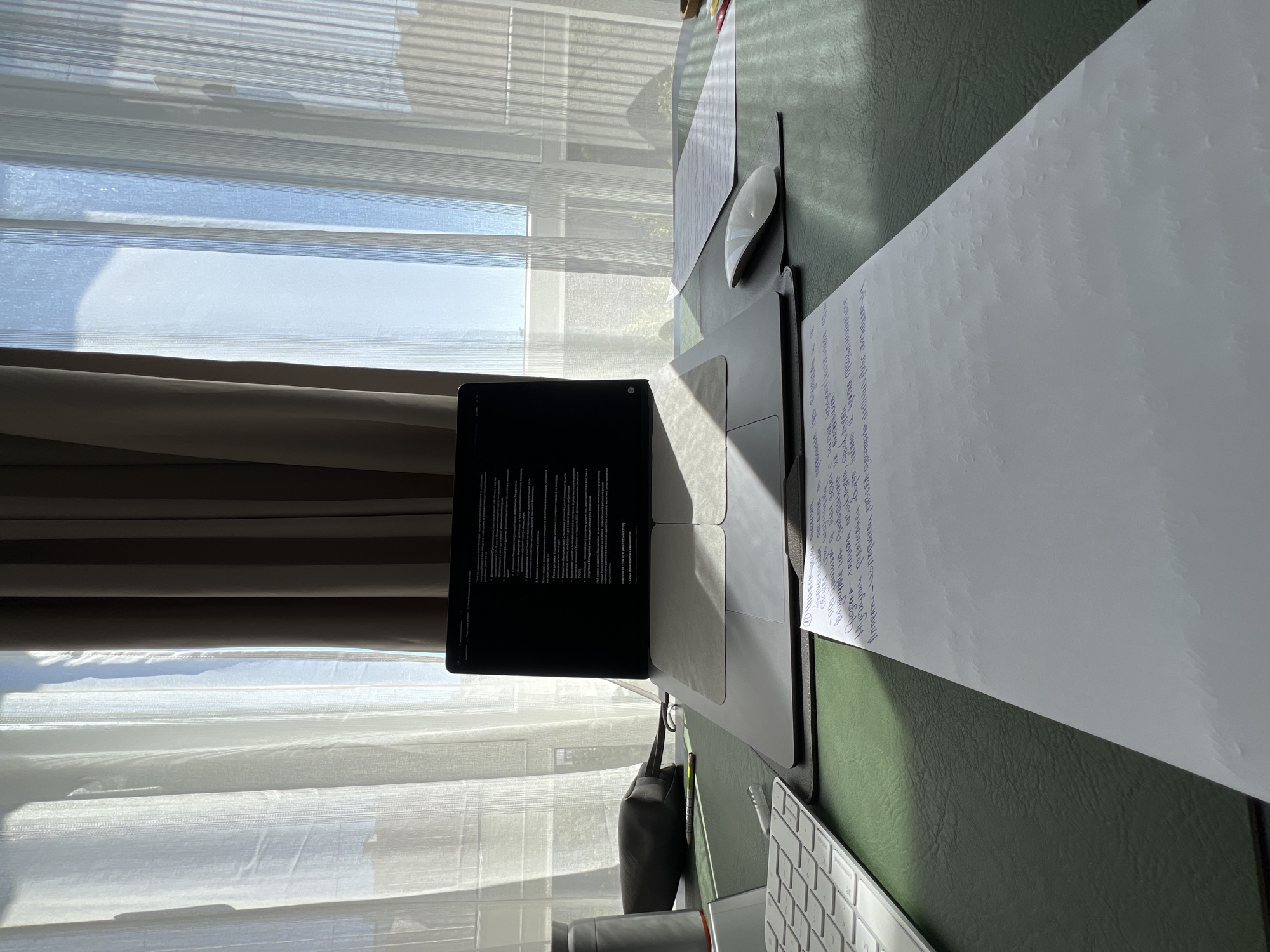 This media file captures a desk scene illuminated by natural light streaming through blinds. The subjects include a laptop, a mouse, a keyboard, papers with handwritten text, and a bag. The scene is set indoors, likely an office or home workspace, with a window providing a view of what appears to be an outdoor environment with some greenery.
The laptop screen displays a document filled with text, suggesting work or study is in progress. Papers are spread across the desk, one of which has blue ink handwriting. A white, ergonomic mouse is positioned next to the laptop, and a white keyboard is visible in the foreground. A dark bag rests on the desk near the laptop.
The lighting indicates it is daytime, with sunlight casting distinct shadows across the desk and the blinds. The sunlight suggests a clear day. The location context of Burgas, Bulgaria, provides a geographical reference, but specific visual cues to confirm this within the image are limited. The overall mood conveyed by the image is one of focused activity and a productive work environment, bathed in natural light. No people are visible in the media file.
Visible text is present on the laptop screen and on the handwritten papers. The text on the laptop screen appears to be a formal document with numbered points and headings. The handwritten text is in a foreign language, likely Cyrillic script, suggesting the location context might be relevant to the content.
