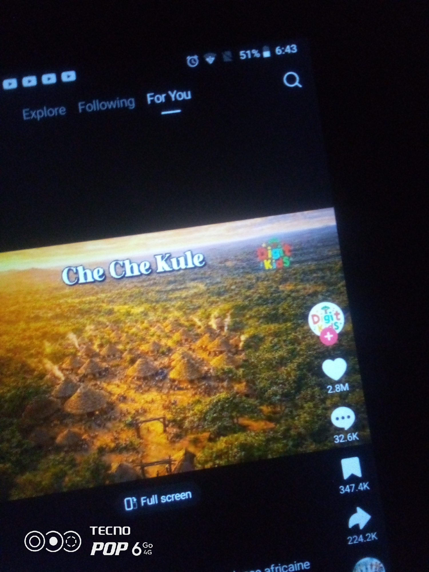 The image shows a close-up view of a mobile phone screen displaying a video. The video appears to be a landscape with thatched-roof structures, possibly a village, set in a lush, green, and golden environment. The text "Che Che Kule" is overlaid on the video in a stylized font. On the right side of the screen, there are social media interaction icons, including a heart with "2.8M" below it, a speech bubble with "32.6K" below it, a bookmark icon with "347.4K" below it, and a share icon with "224.2K" below it. There is also a circular icon with a plus sign and the text "Digit Kids" associated with it. At the bottom left of the screen, a logo for "TECNO POP 6 Go 4G" is visible. The top of the screen displays the time as 6:43 and the battery level as 51%. The top left corner of the screen shows icons related to navigation and possibly notifications. The scene is dimly lit, suggesting it was taken in low-light conditions. There is no discernible information in the image that places it specifically in the city of Howayi, Nigeria.