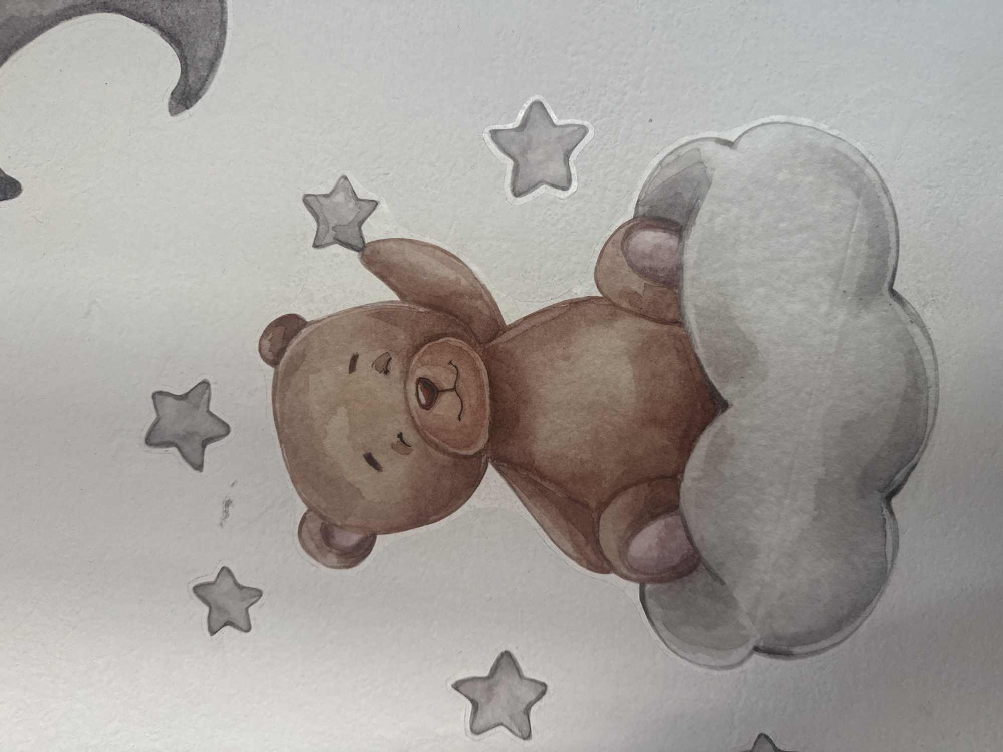A watercolor painting depicts a brown teddy bear sitting on a grey cloud. The bear is holding a small grey star in its right paw, which is raised. Several other grey stars are scattered around the bear. The background is a pale, textured surface, possibly paper or canvas. The painting has a whimsical, childlike aesthetic. There is no indication of the city of Ushtobe, Kazakhstan, or any other location within the image.