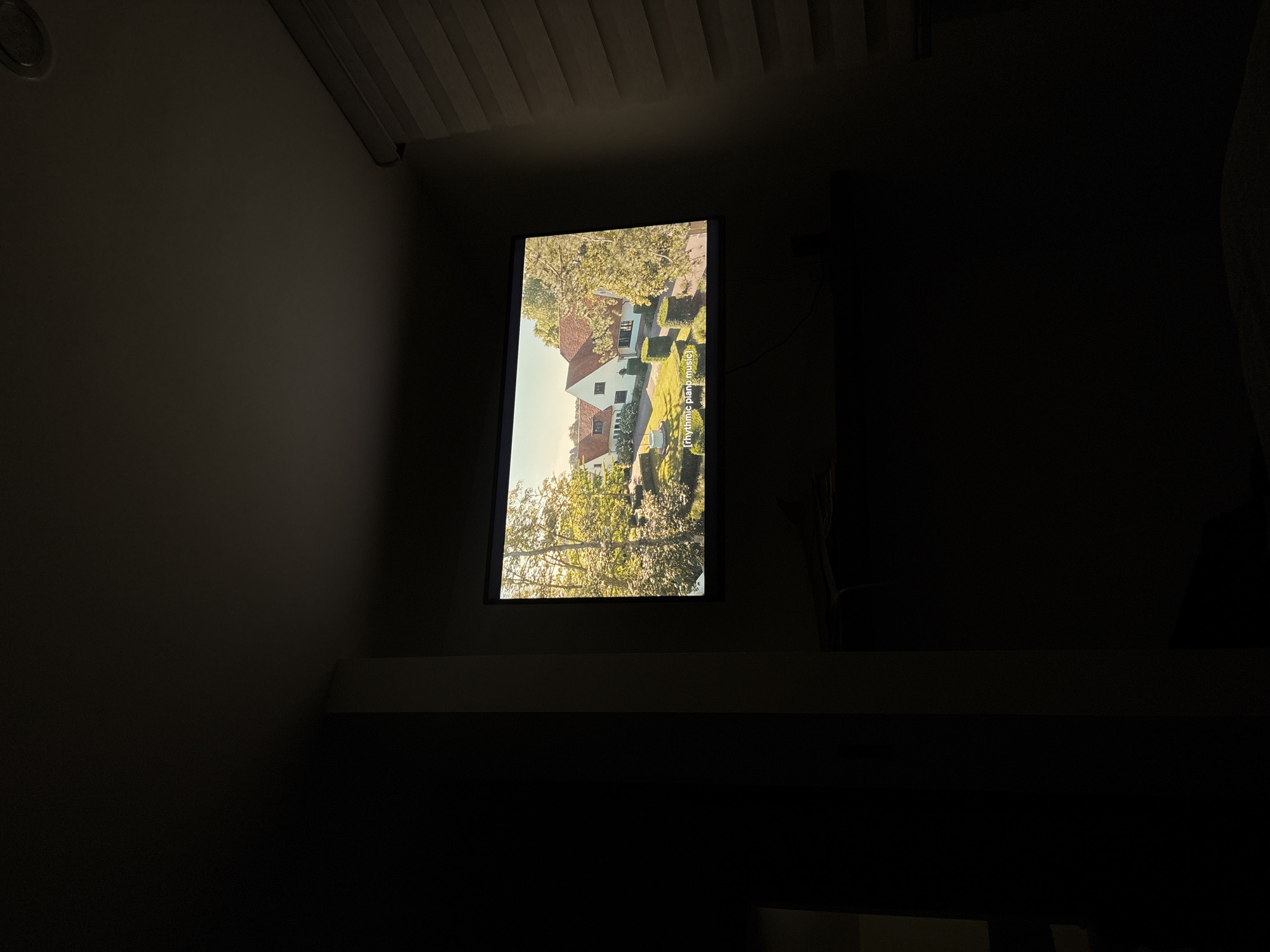 A television screen displays an image of a house amidst greenery. The screen is mounted on a surface, positioned against a dark background. The setting appears to be indoors, in a dimly lit room. The photograph does not provide sufficient detail to determine if the image was taken in San Bernardino Tlaxcalancingo, Mexico.