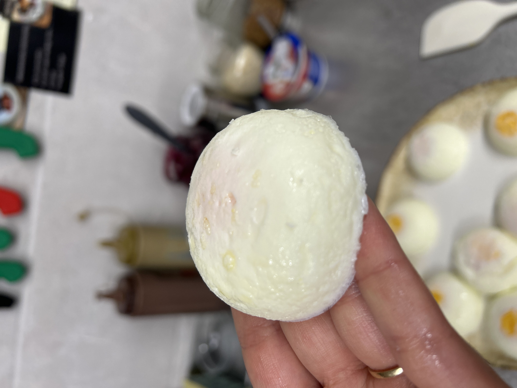 A hand holds a peeled, hard-boiled egg. Other peeled, hard-boiled eggs are on a plate. Condiment squeeze bottles are in the background. The location and city of Burgas, Bulgaria cannot be determined from the image.