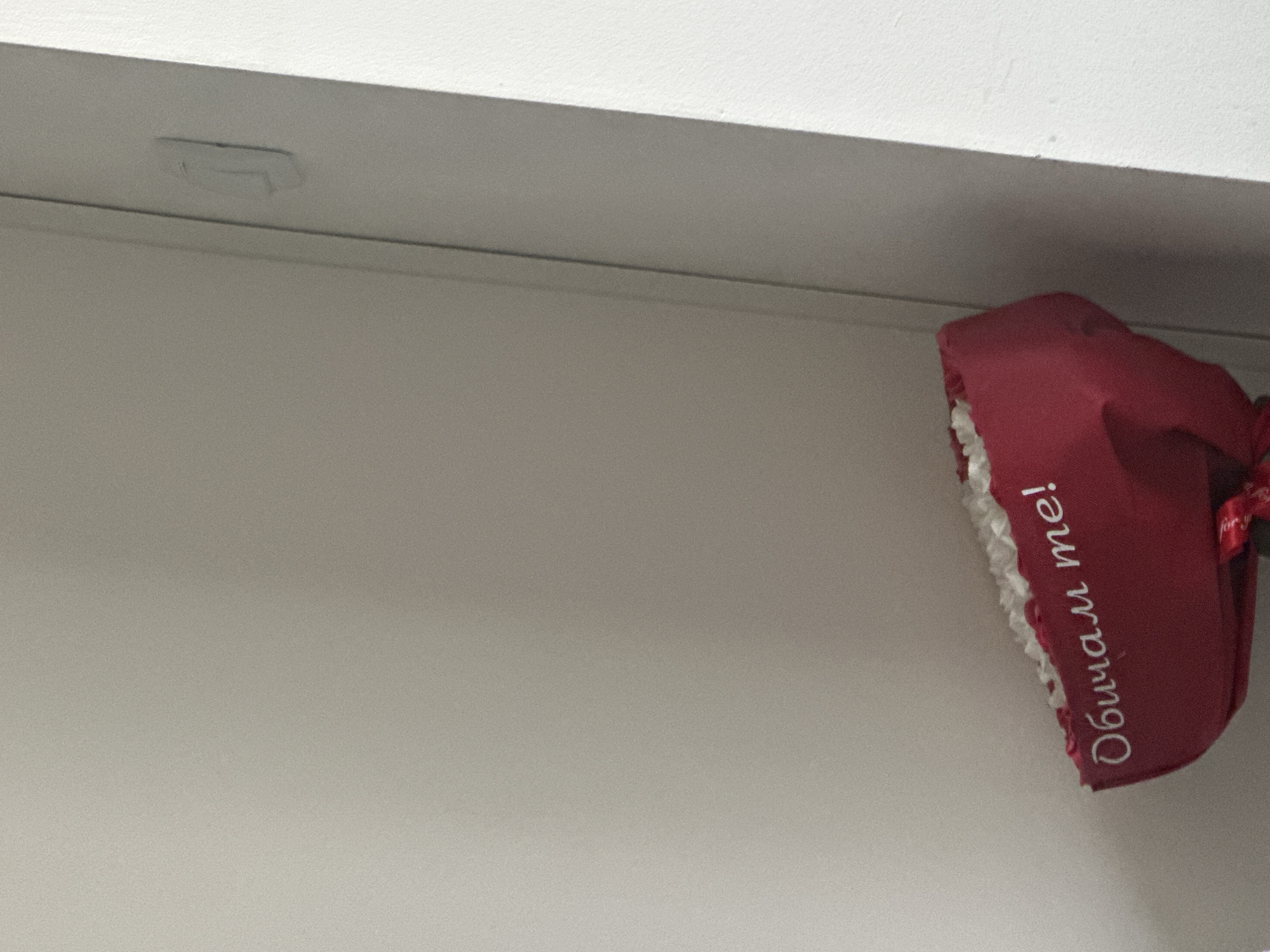 A close-up shot features a red slipper hanging on a white wall. The slipper has white trim and the Bulgarian text "Обичам те!" written on it, which translates to "I love you!". The wall appears to be a part of a building's interior. There is nothing to indicate the precise location in Varna, Bulgaria.
