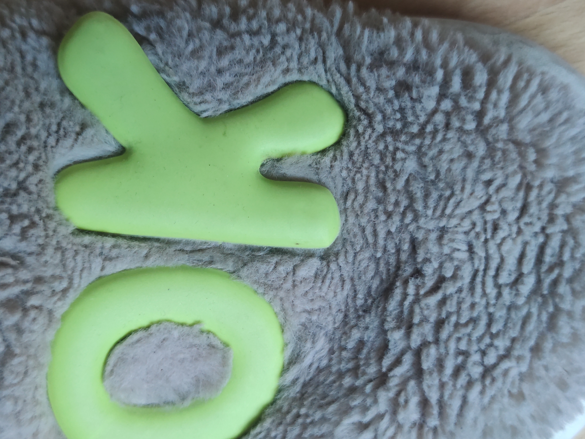 A close-up shot of the letters "XO" in bright green, lying on a grey, fuzzy surface. The location is Unknown, Unknown.