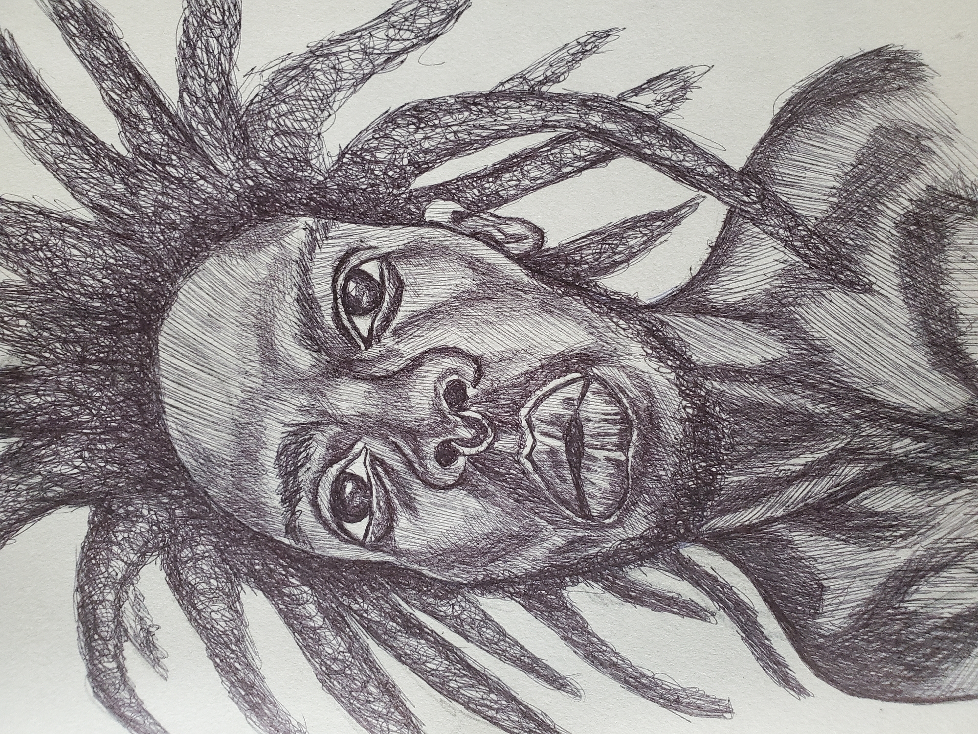 A pen and ink drawing depicts a person with dreadlocks, their head positioned in the center of the frame. The subject is oriented at a slight angle, with their gaze directed towards the viewer. The mouth is partially open, revealing teeth. The overall style of the drawing is characterized by dense cross-hatching and scribbled lines, creating texture and shading. The background is a plain white surface. The location in Mararaba, Nigeria is not depicted or suggested in the image.