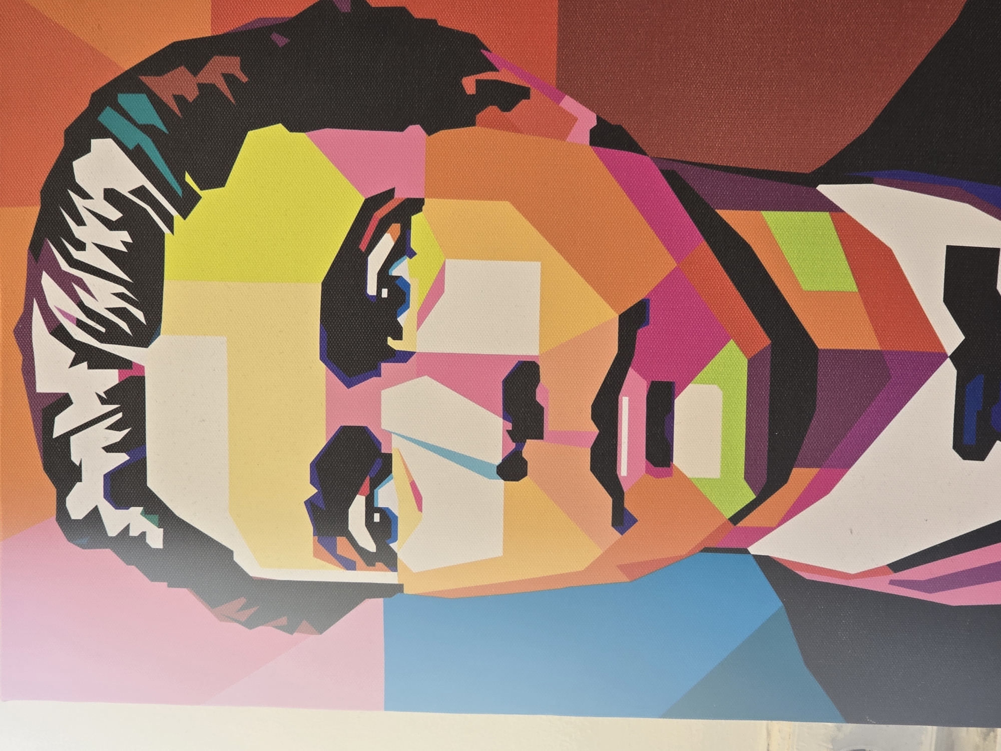 This media file displays a vibrant, highly stylized portrait of a person, likely male, rendered in the Wedha's Pop Art Portrait (WPAP) style. The artwork is characterized by its distinct geometric facets, sharp lines, and bold, flat areas of contrasting colors, entirely devoid of curves or gradients.
The subject's head is depicted slightly tilted, looking upwards and to the right. The face is a mosaic of numerous bright and saturated hues, including various shades of yellow, orange, pink, purple, blue, green, red, black, and white/cream tones. Prominent black outlines define many of the facial features, such as the eyes, nose, mouth, and the contours of the face and hair. The hair appears dark, featuring geometric highlights in teal and white. The visible canvas texture across the entire image suggests it is a print on canvas or an original painting.
There is no specific activity or event taking place; it is a static artistic portrait. The background is also composed of geometric color blocks that complement the overall aesthetic of the subject. No specific location cues, time of day, weather, emotions, or visible text are discernible within the artwork.