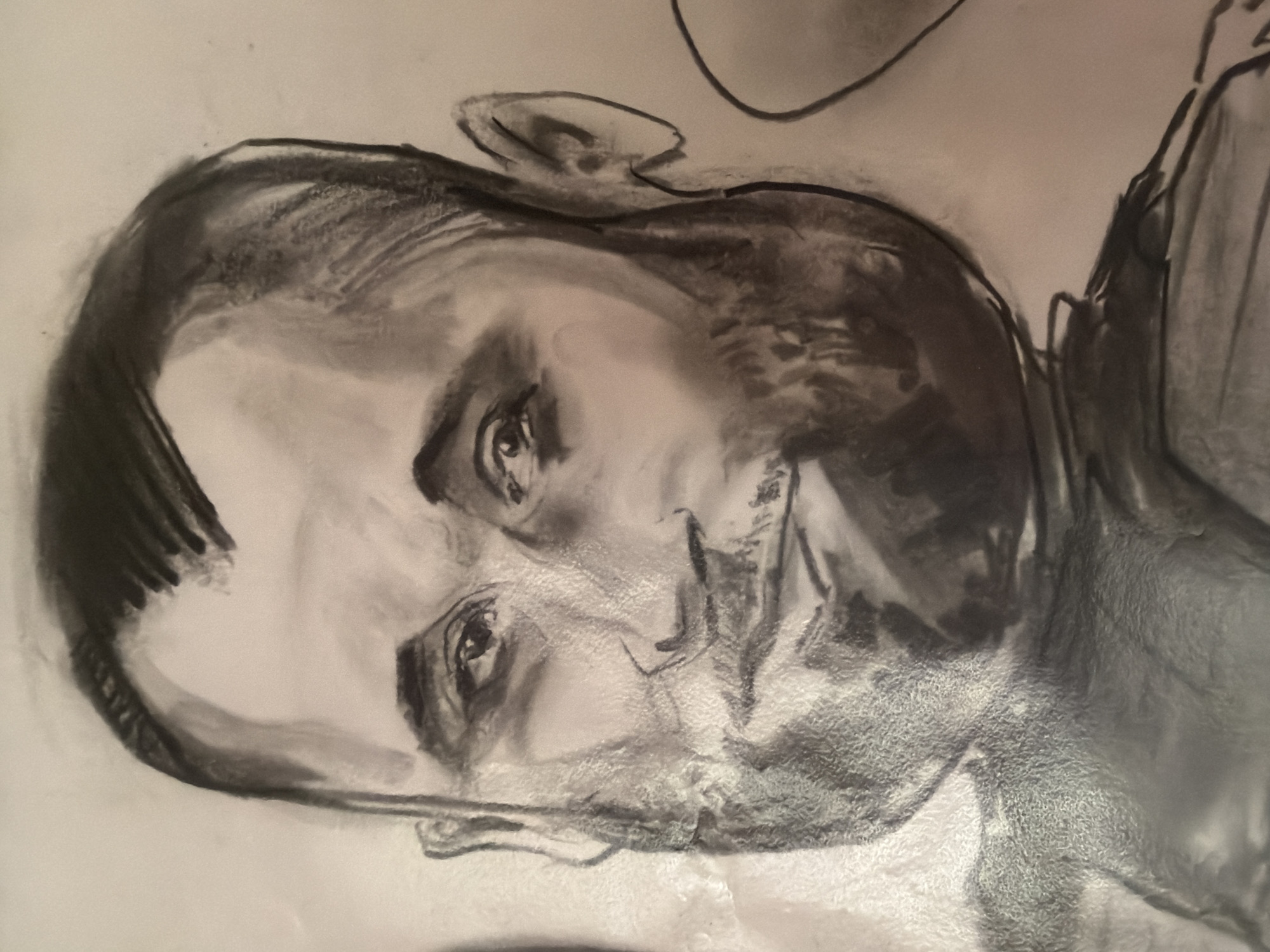 This is a charcoal drawing of a man's head and shoulders. The man has short, dark hair slicked back, a full beard, and a mustache. He is looking slightly off-camera to his right with a neutral expression. The drawing is done in a realistic style with heavy use of shading to create depth and form. The background is plain and white, suggesting the drawing is on paper. There is no identifiable urban or rural environment depicted; therefore, its location in Папярнянскі сельскі Савет, Belarus cannot be determined from the image alone. The drawing appears to be a portrait, likely a study or a finished artwork.