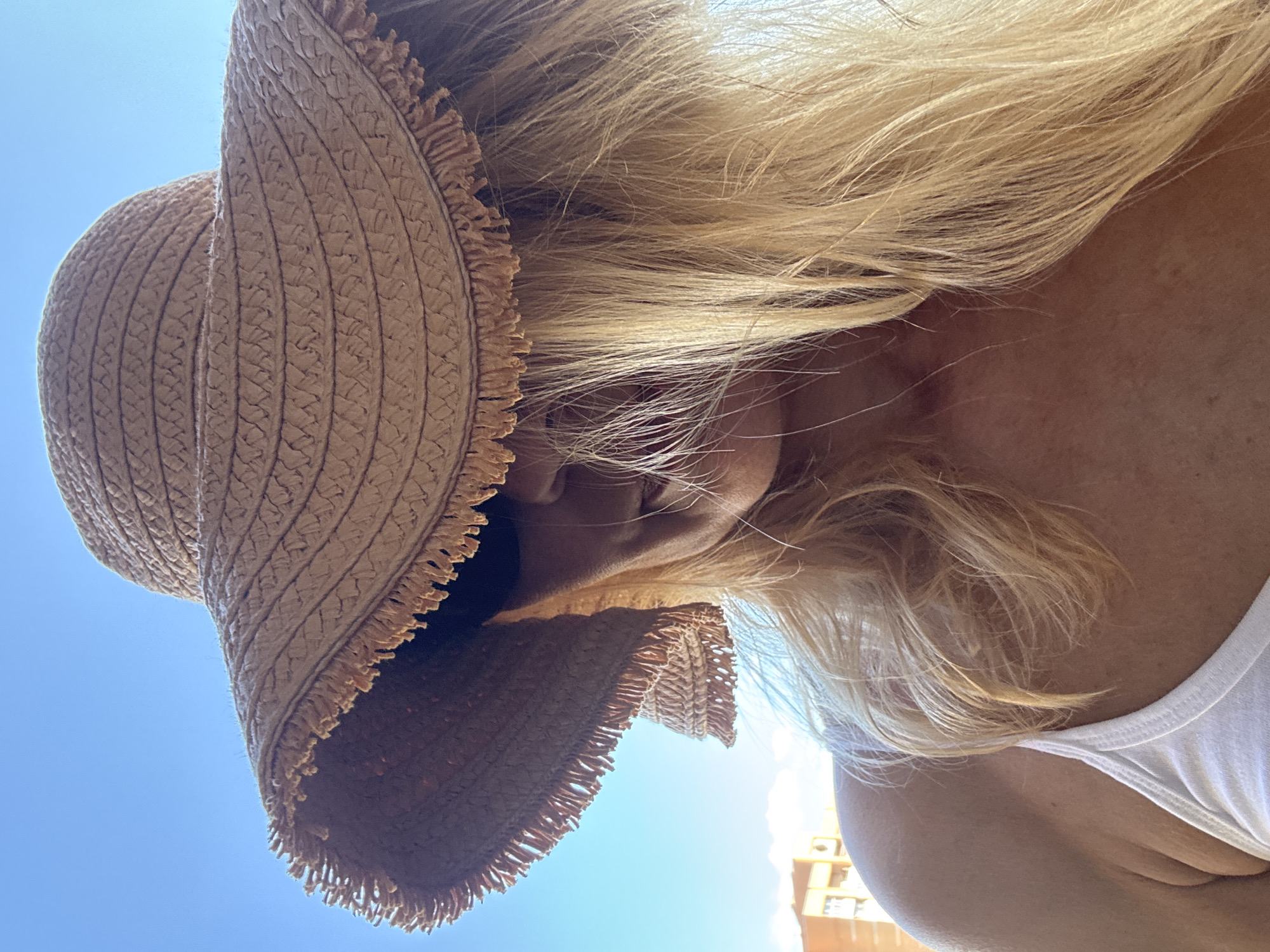 A low-angle, slightly tilted shot depicts a person wearing a straw hat, with blond hair visible beneath it. The sky is visible in the background. A building is also visible in the background. The person is wearing a white top. The image provides no information about the city of Minsk, Belarus.