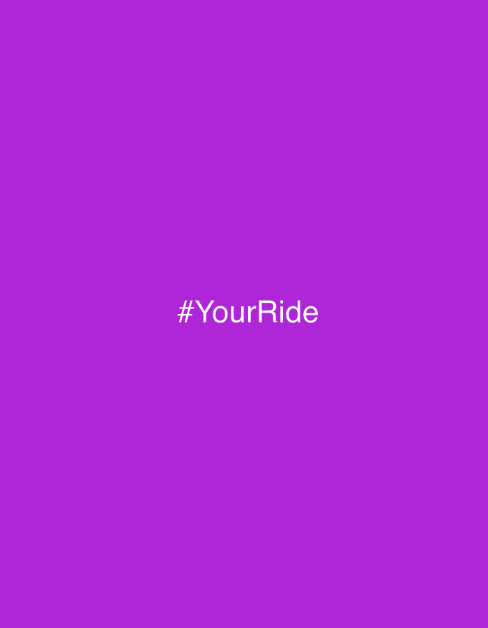 The image displays a solid, vibrant purple background. Centered on this purple field is white text that reads "#YourRide". There are no other subjects, objects, people, or discernible activities present in the image. The setting is minimalist, consisting solely of the colored background and the text. No specific time of day, weather conditions, or detailed location cues are visible within the image content.