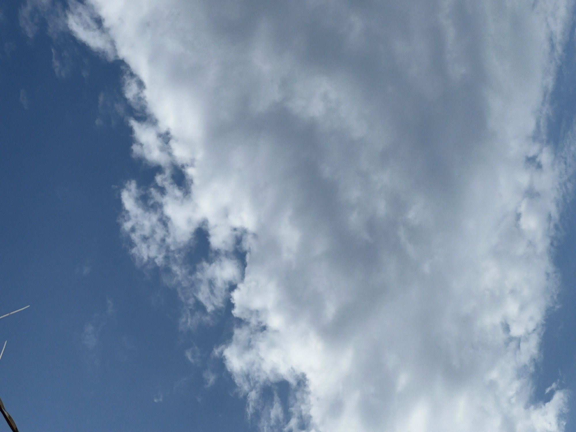 The image depicts a sky with clouds. There are two thin, white, rod-like objects partially visible in the upper left corner of the frame, extending downwards and to the right. They appear to be attached to something out of frame. The sky is a deep blue, with scattered white and gray clouds. The clouds are dense and fluffy, with some appearing darker and more shadowed than others. The overall impression is of a partly cloudy day. There are no people, animals, or structures visible within the frame, and the scene appears to be outdoors. The location is identified as Golubitskaya, Russia.