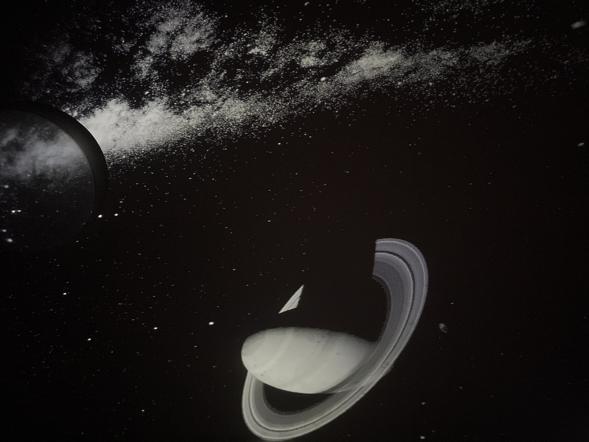 The image shows a projection of Saturn with its rings against a dark background. There are also projections of stars and what appears to be a nebula or galaxy. The scene is likely in a planetarium or educational facility. There is no information in the image to indicate its location in Chaikovsky, Russia.