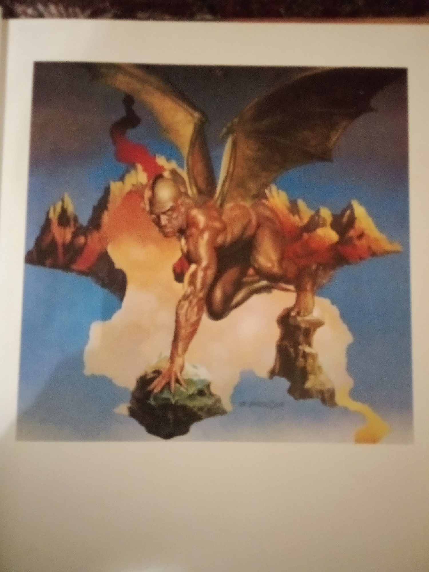 The image is a painting depicting a muscular, winged humanoid figure with leathery wings, crouched on a rocky outcrop in a surreal landscape. The figure has a bald head and is looking down towards its hands, which are gripping another rock. Behind the figure, floating islands with rocky formations are visible against a blue sky with swirling clouds. The overall impression is one of fantasy and power. There is no discernible location in the city of Zhmerynka, Ukraine, depicted in this image.