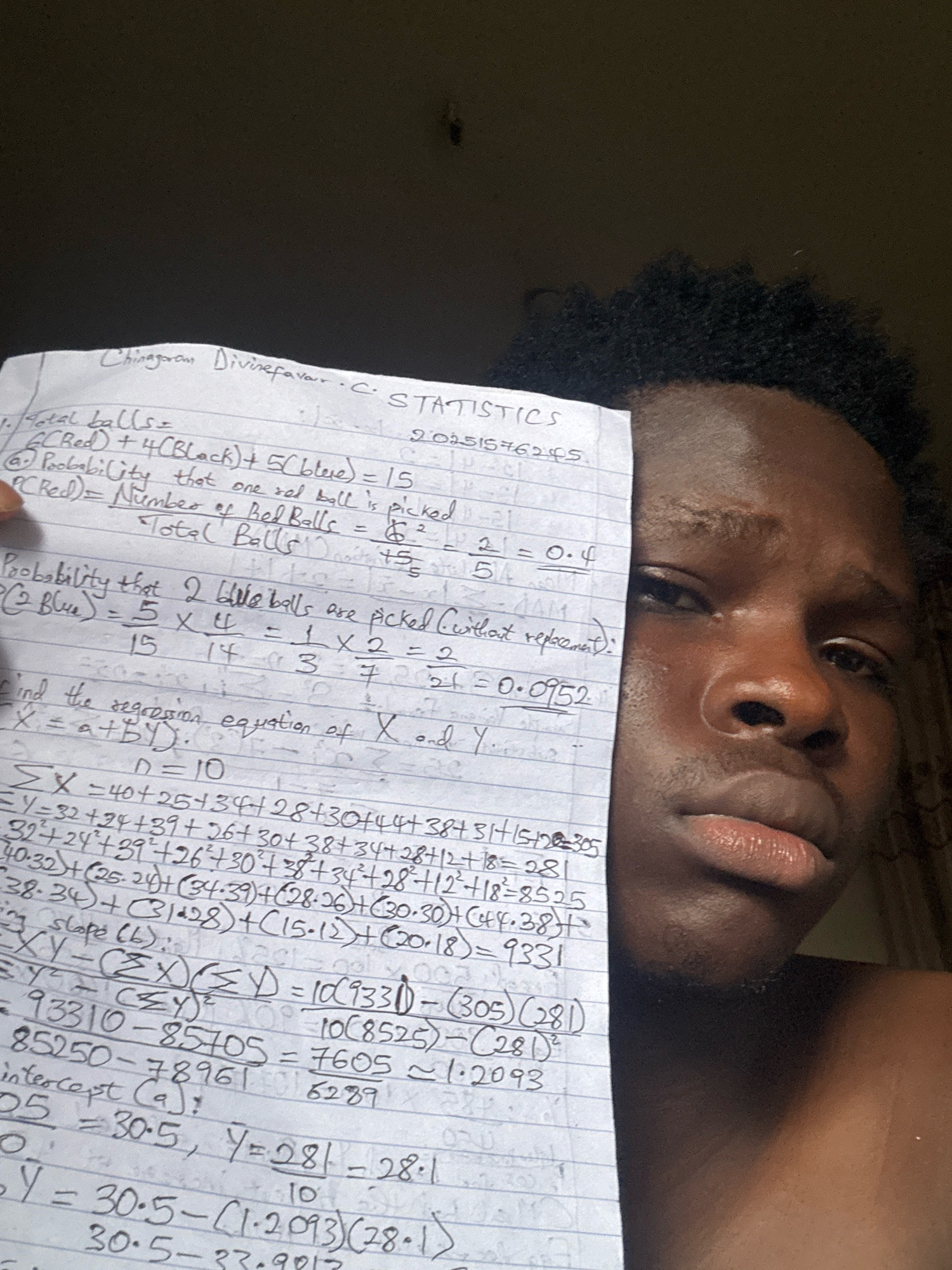 The image shows a young man in the city of Ihiagwa, Nigeria, holding a piece of paper with handwritten math problems related to statistics. The man has dark skin and short, dark, curly hair. He is looking towards the camera with a neutral expression. The paper is partially obscuring his face and chest. The background is dark and out of focus, but appears to be an indoor setting. The math problems involve calculations of probabilities and regression equations. The text on the paper includes headings such as "STATISTICS", "Total balls", and "Probability that 2 blue balls are picked (without replacement)". There are also several equations and numerical calculations visible. The lighting suggests it might be daytime, possibly with indoor lighting.
