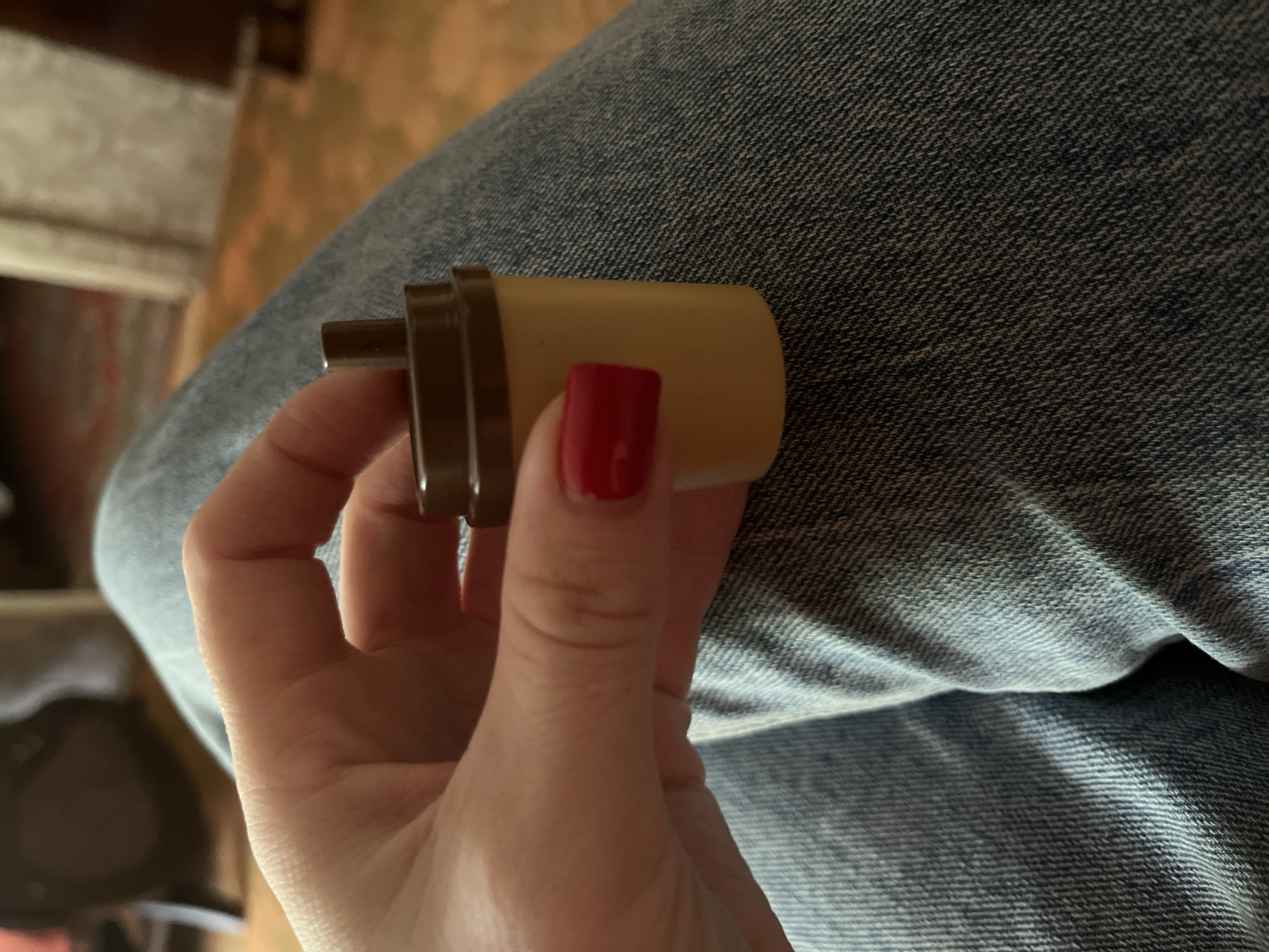 A person is holding a cylindrical object. The object is tan colored with brown accents. The person's fingernails are painted red. The person is wearing blue jeans. The background is blurry and indistinct. There is no information given about the city of Chaikovsky, Russia.