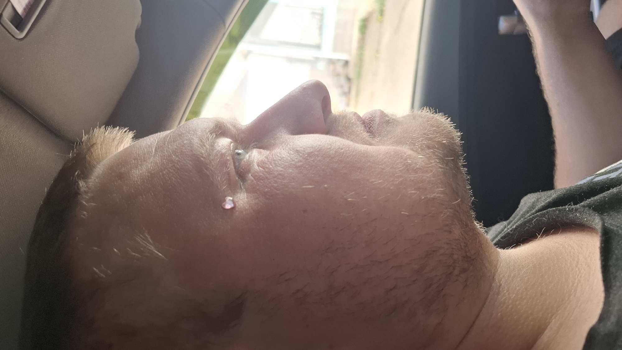 A man is seen in profile, his head tilted back, with a tear on his cheek. He appears to be inside a car, as the interior and a glimpse of the outside are visible in the background. The location is not identifiable as Chaikovsky, Russia, based on the visual information in the image.