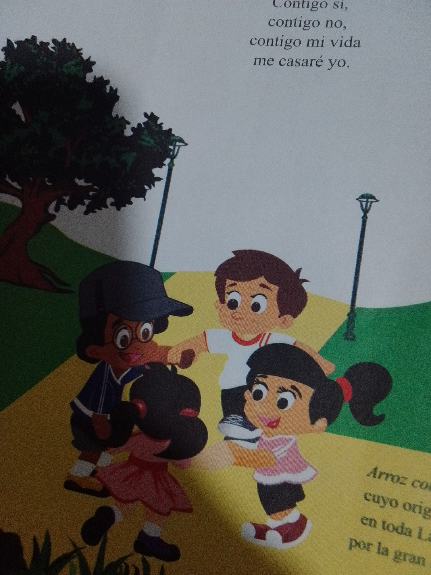 The image is an illustration featuring four cartoon children in a park-like setting. On the left, a child wearing a dark blue jacket and a black baseball cap with glasses stands with their arms around another child who is wearing a pink dress and has a red hair tie. To the right of these two children, a boy in a white shirt with a red collar and dark hair is reaching out his hand. A lamppost stands behind the boy. The background depicts a tree with dark foliage and a path that transitions from yellow to green. The overall scene appears to be a daytime illustration, possibly from a children's book, depicting children interacting. There is no information or visual element within the image that suggests a specific location in La Tagua, Venezuela.