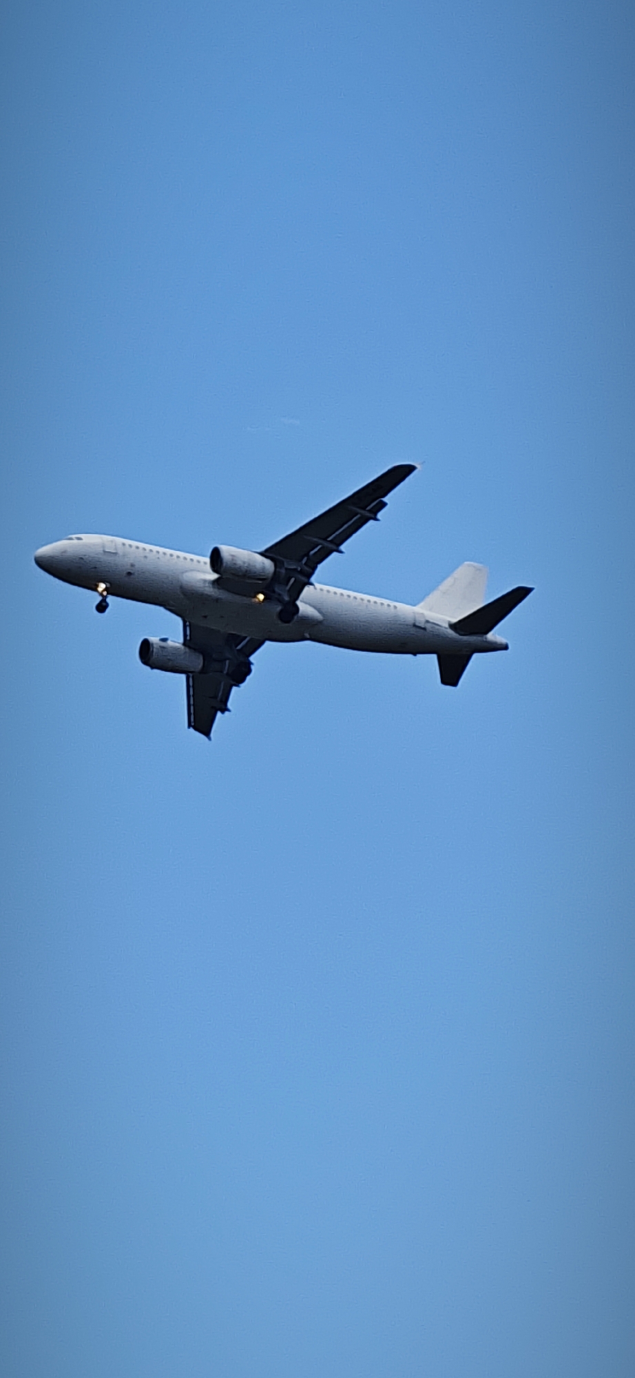 An airplane is in the sky. The plane is facing towards the upper left corner of the image. It has its landing gear down and lights on. The sky is light blue. The location is Burgas, Bulgaria.