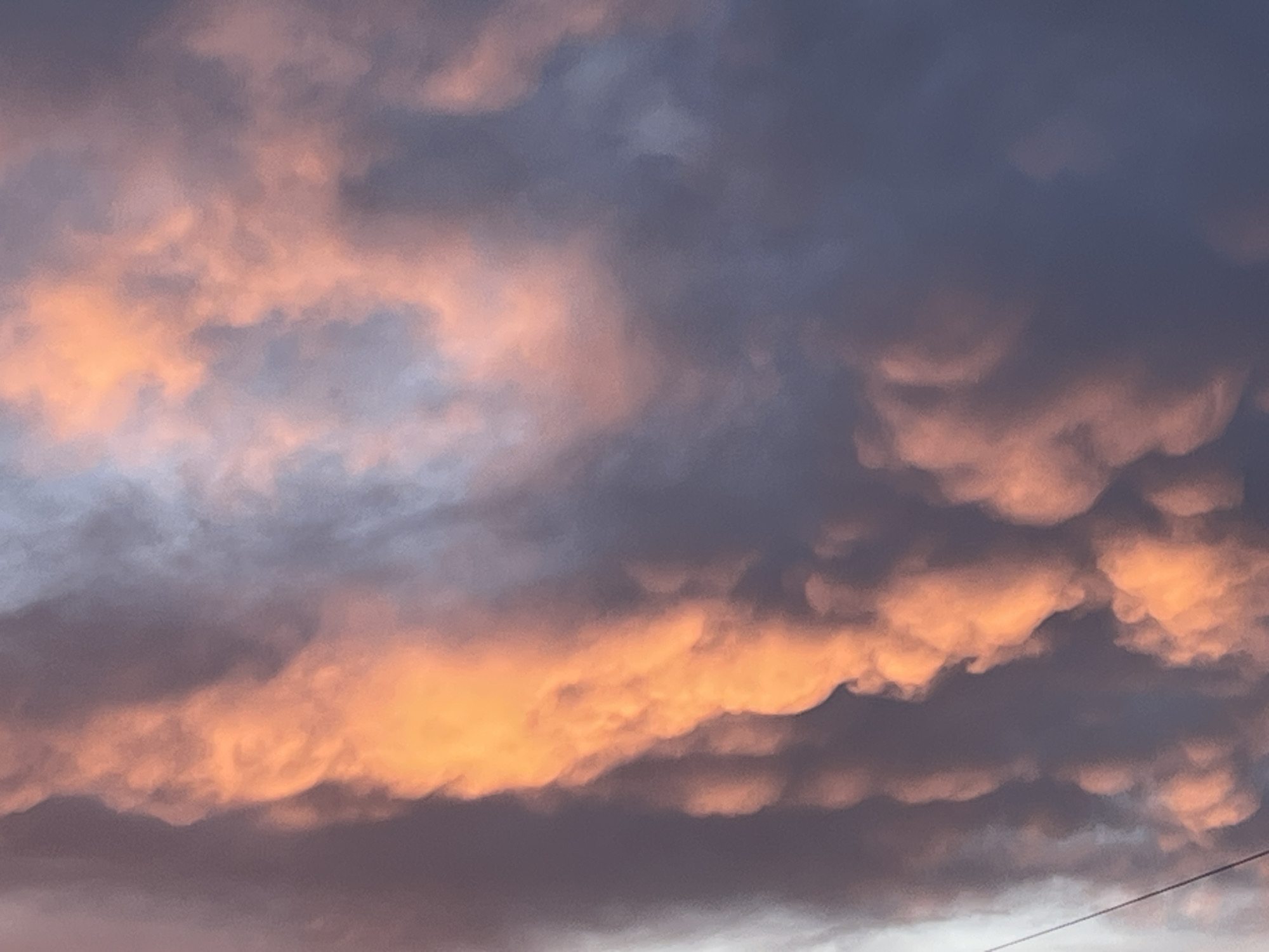 The image shows a sky with mammatus clouds, displaying a sunset with orange and gray hues. The location is unspecified, but claimed to be in Pchelnik, Bulgaria. A power line is visible in the lower right corner.