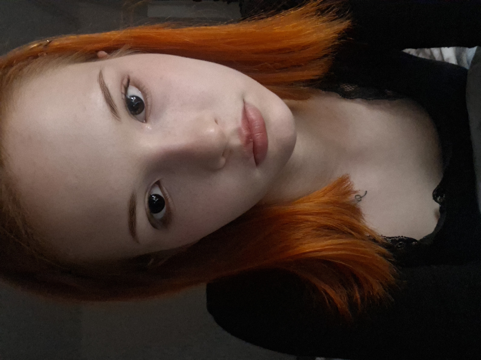 A photograph shows a young woman with orange hair. Her face is pale, and she has dark eyes and light eyebrows. She appears to be wearing a black top with lace detail. The background is dark and indistinct. There is no indication of the location being Chaikovsky, Russia.