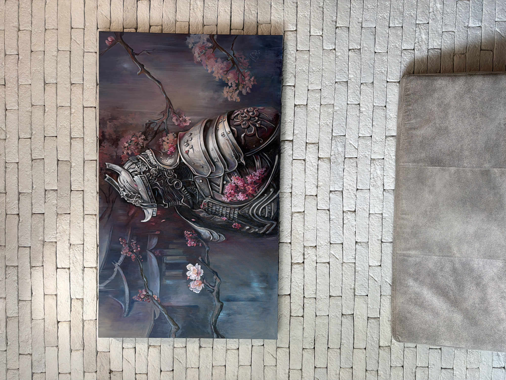 The image shows a painting of a samurai helmet adorned with cherry blossoms, hanging on a white brick wall in Varna, Bulgaria. To the right of the painting is a gray upholstered object, possibly part of a couch or chair. The location is indicated by metadata or specific local features visible in the full context, but is not identifiable in the immediate cropped views.
