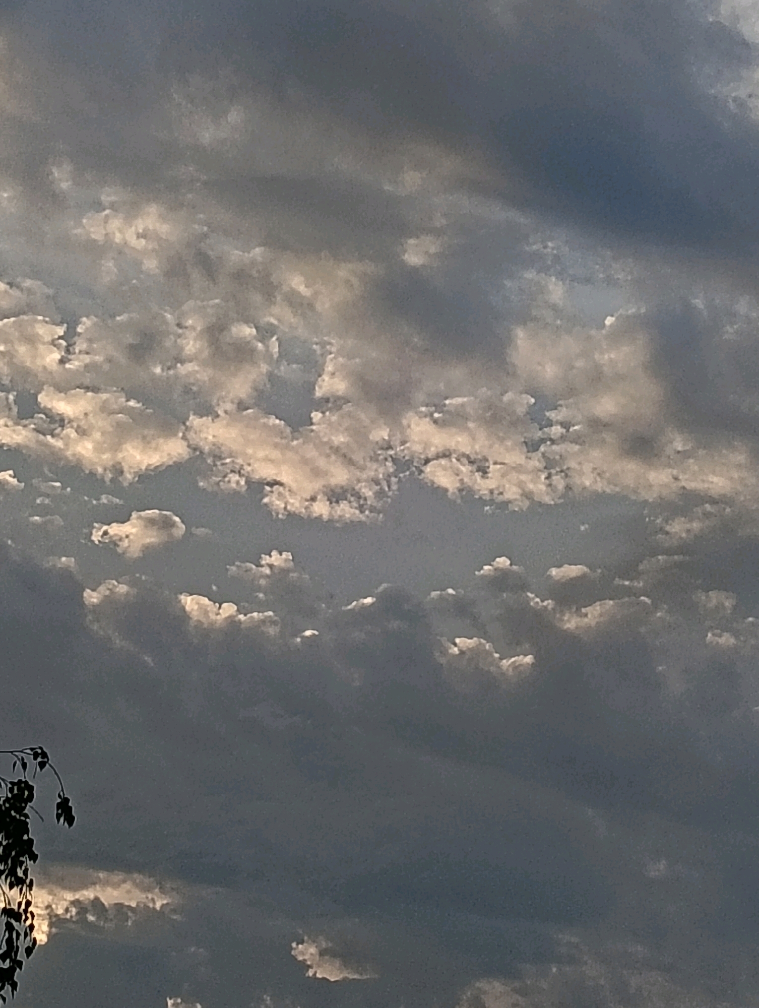 The image shows a cloudy sky with dramatic lighting. The clouds are a mix of dark gray and white, with some areas appearing brighter where sunlight is breaking through. The sky is overcast, suggesting it may be early morning or late afternoon. There are no people or specific landmarks visible in the image. The composition is focused solely on the sky and clouds. The general atmospheric conditions suggest a temperate climate, potentially with varying weather patterns.