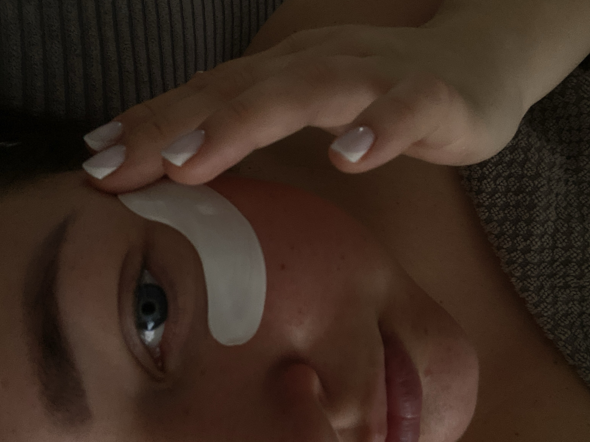 A close-up image shows a person with fair skin lying down, receiving what appears to be a cosmetic or beauty treatment. A white, semi-circular patch is positioned under the person's left eye. The person's blue eye is open. A hand with white-tipped fingernails is resting on the person's forehead. The subject is lying on a grey textured material. The image does not provide information about the location in the city of Sochi, Russia.