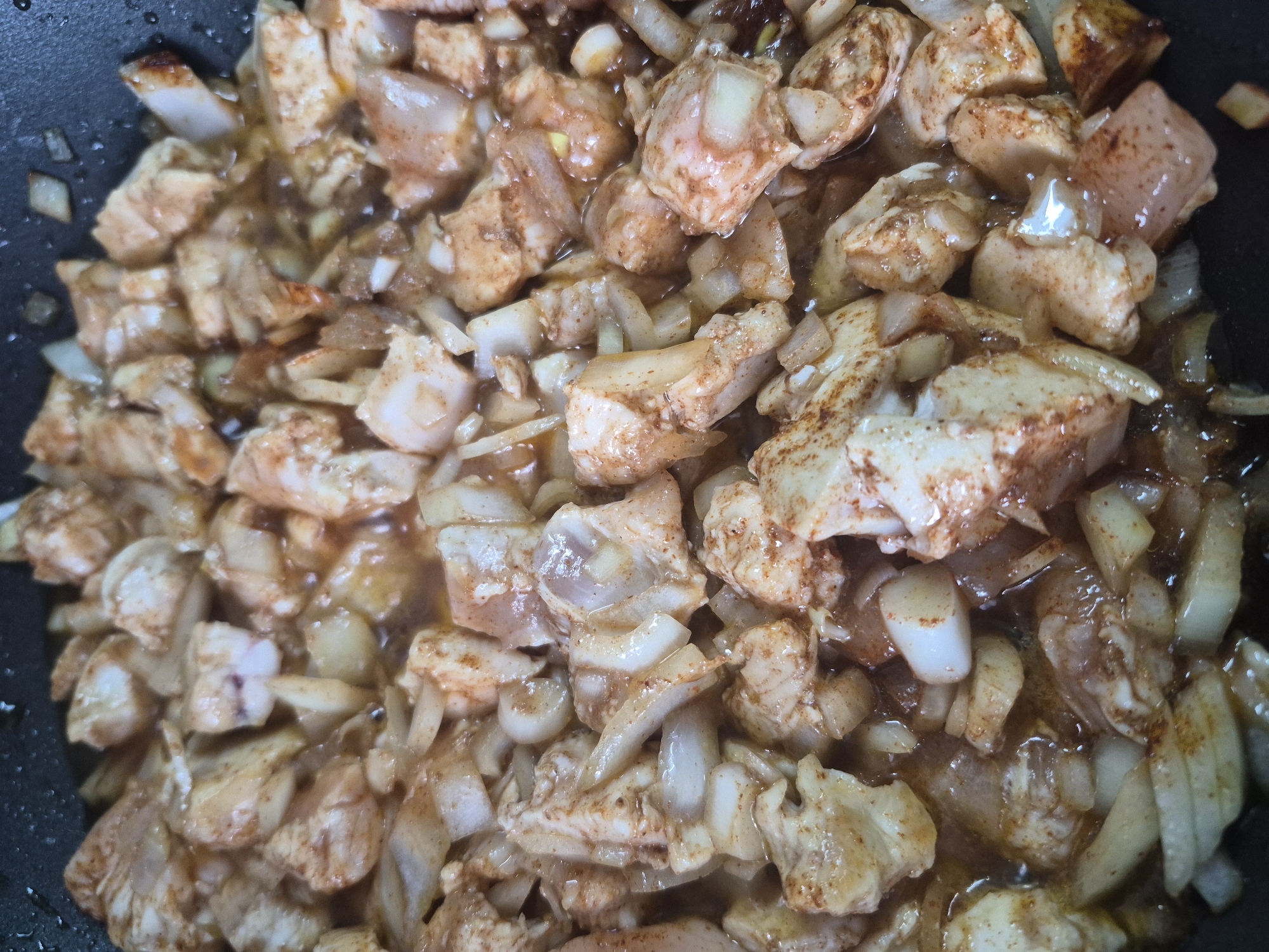 The image shows a close-up of diced chicken and onions being cooked in a pan. There is no indication of Tobolsk, Russia, people, or specific actions beyond the cooking process. The environment is limited to the cooking pan and its contents.