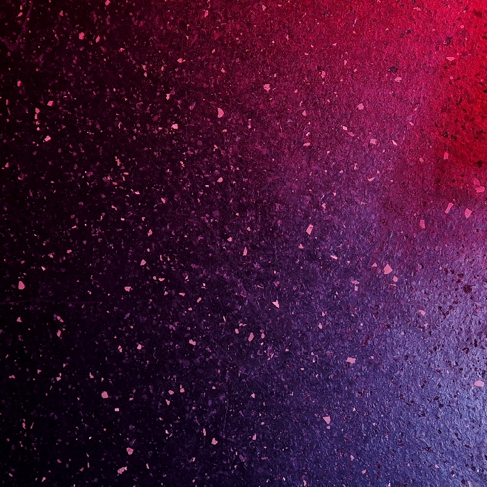 The image depicts a granular, textured surface, likely pavement or a composite material, featuring numerous irregularly shaped, light-toned flecks distributed across its dark ground. A prominent color gradient illuminates the surface, transitioning from deep blue-purple in the bottom-left corner through various shades of purple, culminating in dark magenta and deep red towards the upper-right. No individuals, identifiable objects, or specific actions are depicted within this scene, which is situated in Strasbourg, France.
