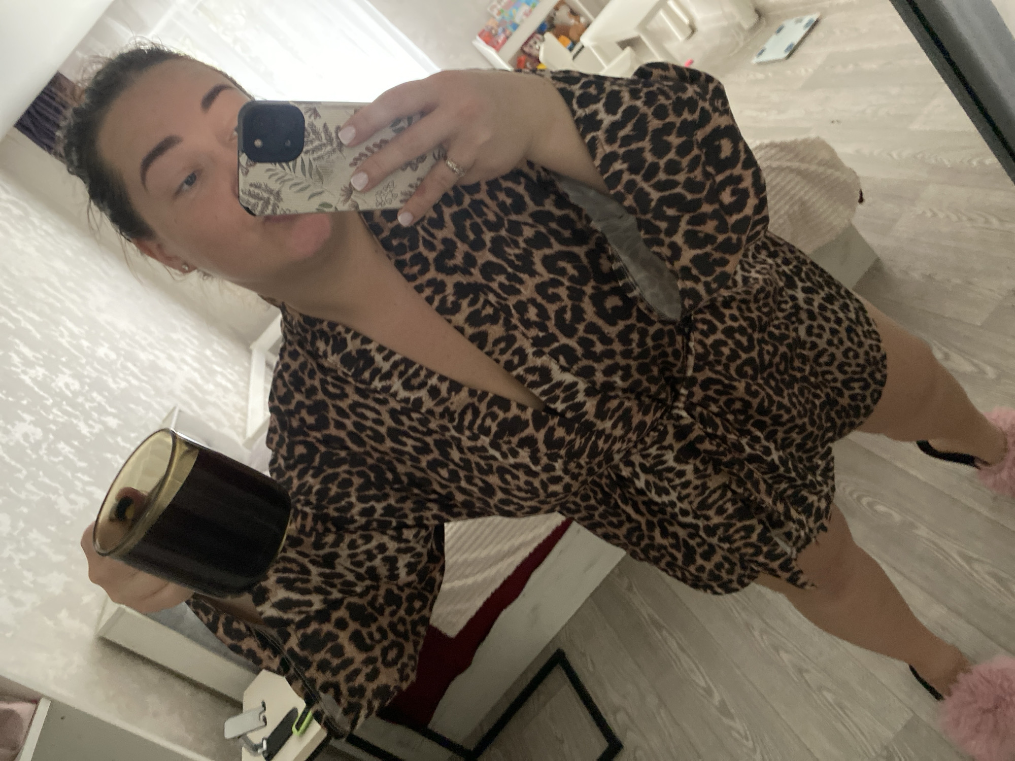 A woman in a leopard-print robe holds a black candle while taking a selfie in front of a mirror. The location appears to be a domestic interior, likely a bedroom, based on the presence of a bed and other furniture. There is no information available in the image to identify the location as Sochi, Russia.
