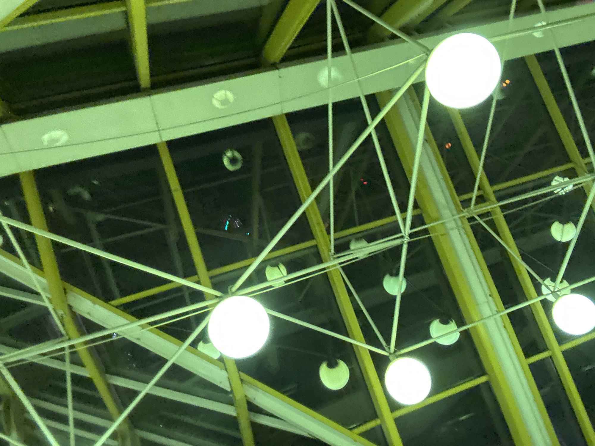 The image depicts a ceiling structure with yellow beams and white support rods. There are multiple round lights hanging from the ceiling, some illuminated. The background appears dark. The location is unknown.