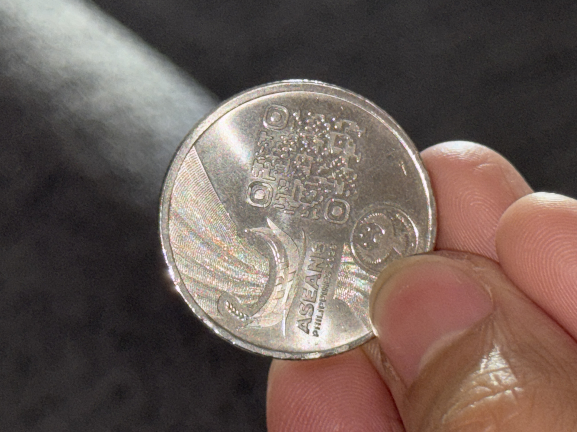 A hand is holding a Philippine coin. The coin features a QR code, the ASEAN logo, and the text "PHILIPPINES 2023." The location, Davao City, Philippines, cannot be determined from the image.