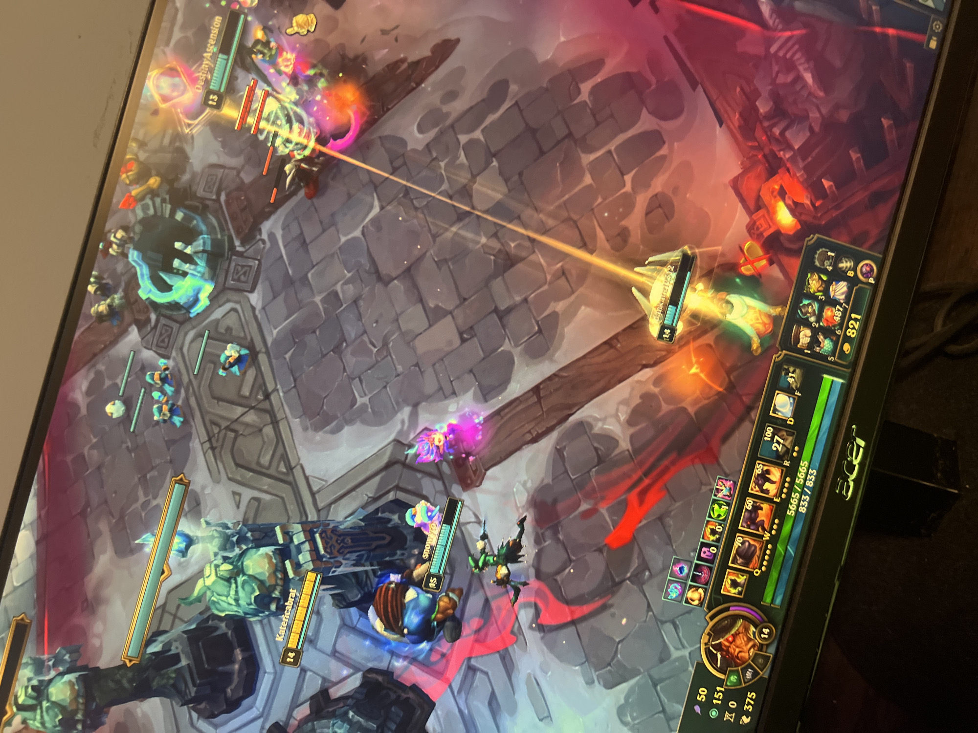 The image shows a computer screen displaying a game of League of Legends. The game is in progress, with champions engaging in combat. The team on the bottom-left corner includes a champion named "Katericabrat" at level 14, while the opposing champion is named "DestinyAscension" at level 13. Minions are visible, and the environment appears to be a typical map from the game, with stone pathways and structures. No location in Burgas, Bulgaria, is apparent in the scene.