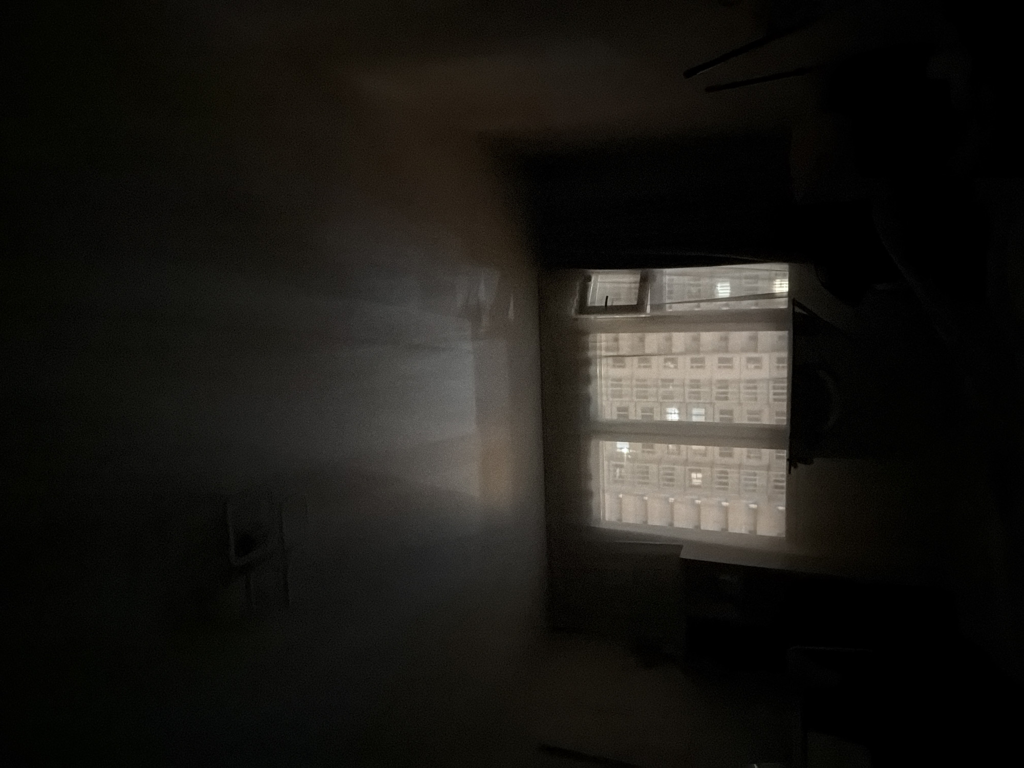 The interior of a darkened room is viewed through a window in Saint Petersburg, Russia. Outside the window is a densely built-up area consisting of other buildings. The room is dark, with the only visible light coming from the window. An electrical outlet is visible on the wall.