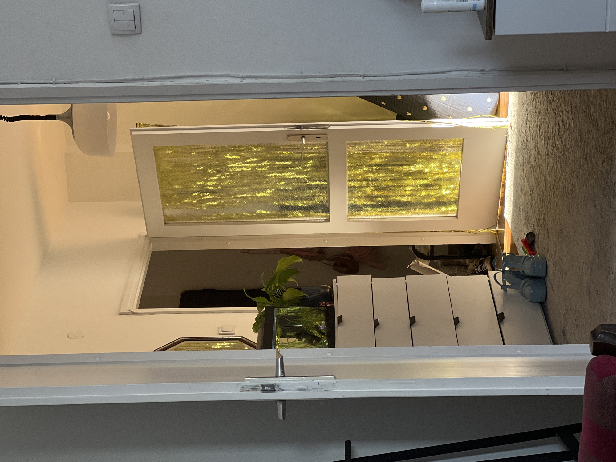 A view through an open doorway shows a room beyond. The doorway is white and the door is ajar, revealing a room with white furniture, including a chest of drawers and what appears to be a fish tank with plants. The room also contains a rug or carpet. The location cannot be determined from the image.