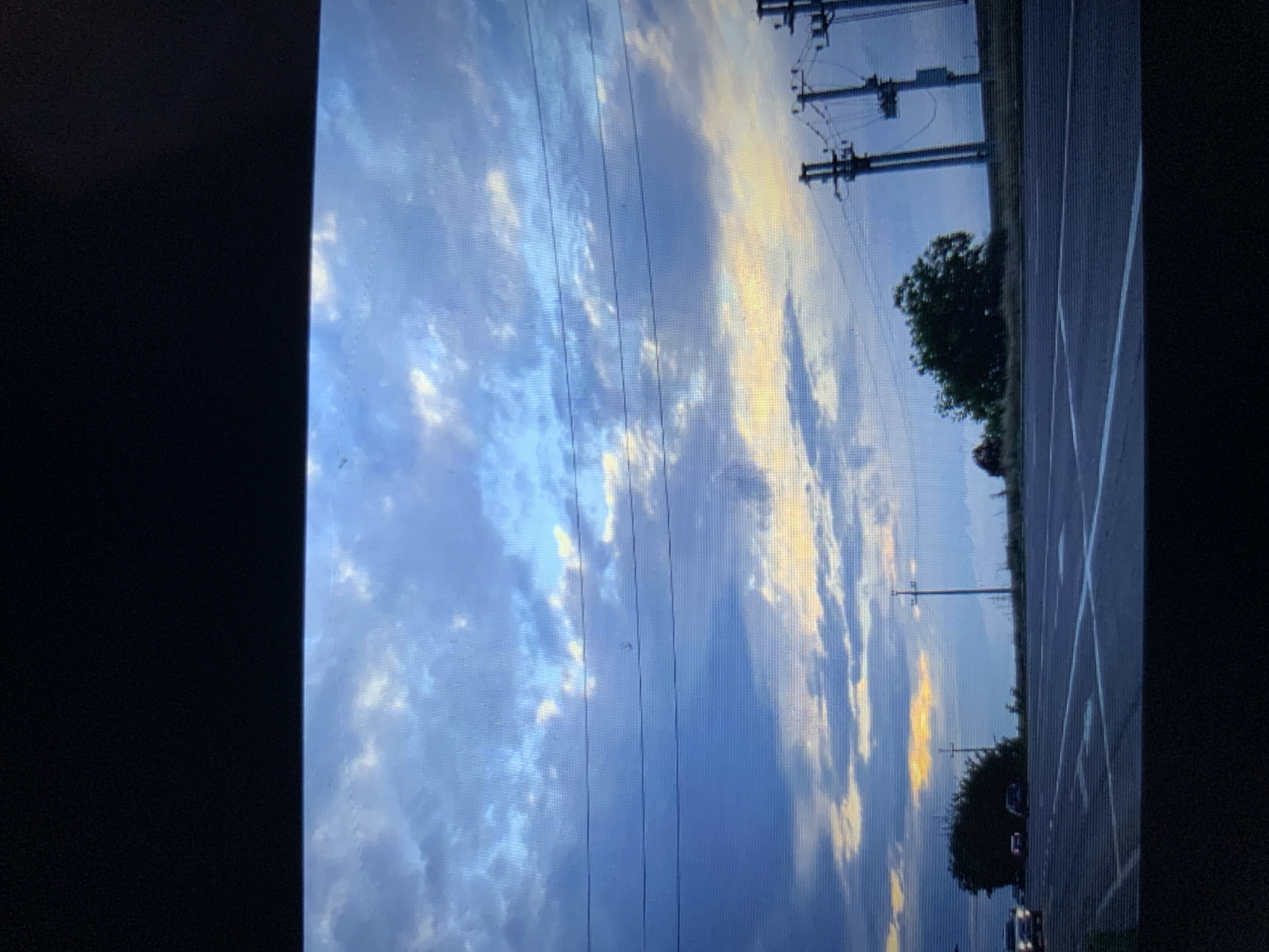 The image captures a wide shot of a road with a cloudy sky. In the distance, there are power lines and poles. A few cars are visible on the road, and some trees and bushes are on the side. The lighting suggests it could be early morning or late evening, given the colors in the sky. There is no indication of the specific location within Lymanka, Ukraine.