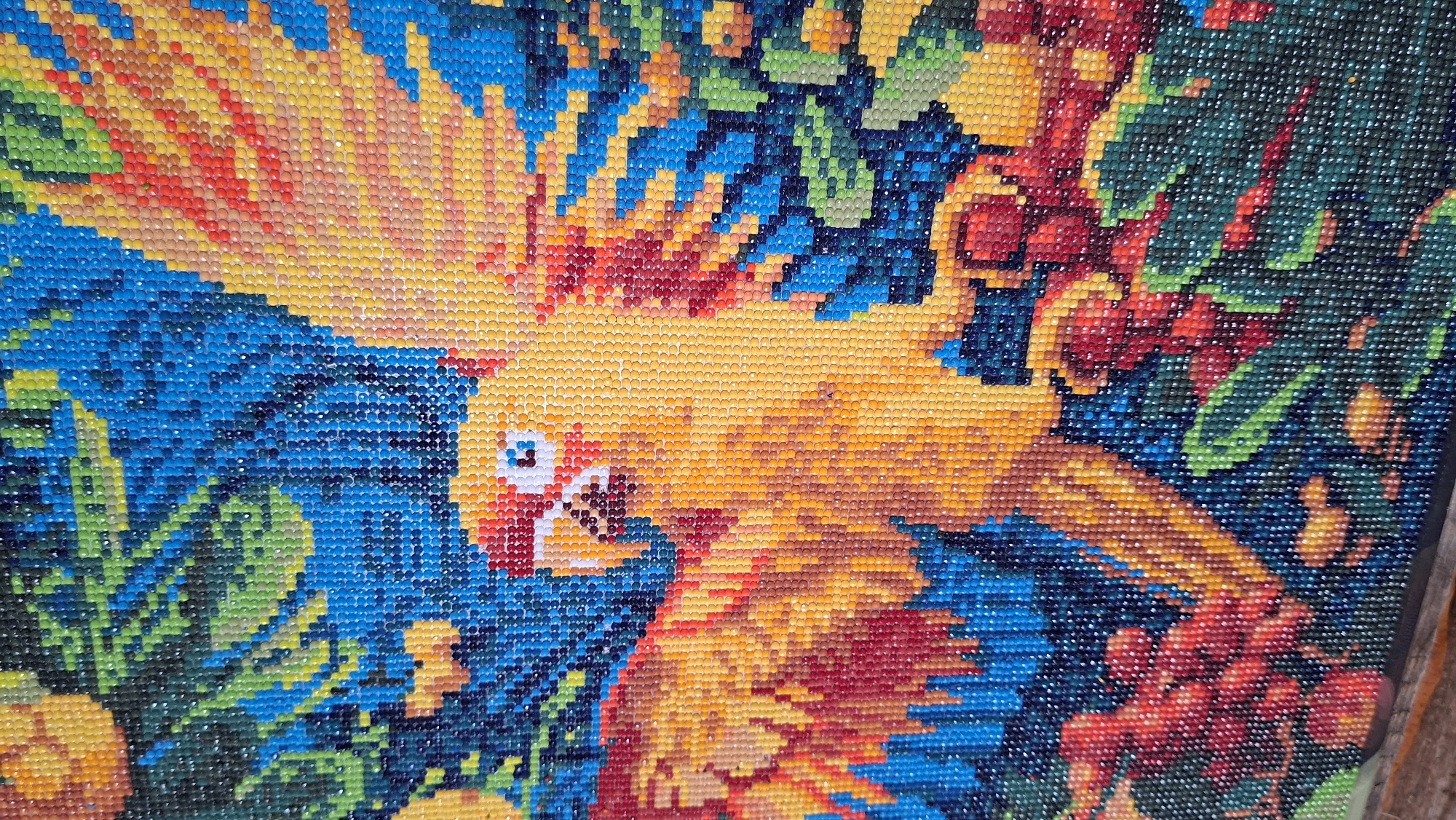This image appears to be a close-up of a diamond painting featuring a colorful parrot. The parrot is predominantly yellow with red and orange accents on its wings and body. It is set against a background of blue and green, with some areas resembling foliage and berries. The entire image is composed of small, faceted diamond-like beads, giving it a pixelated appearance.
I cannot extract from the image any information linking to the city of Большой Букор, Russia.