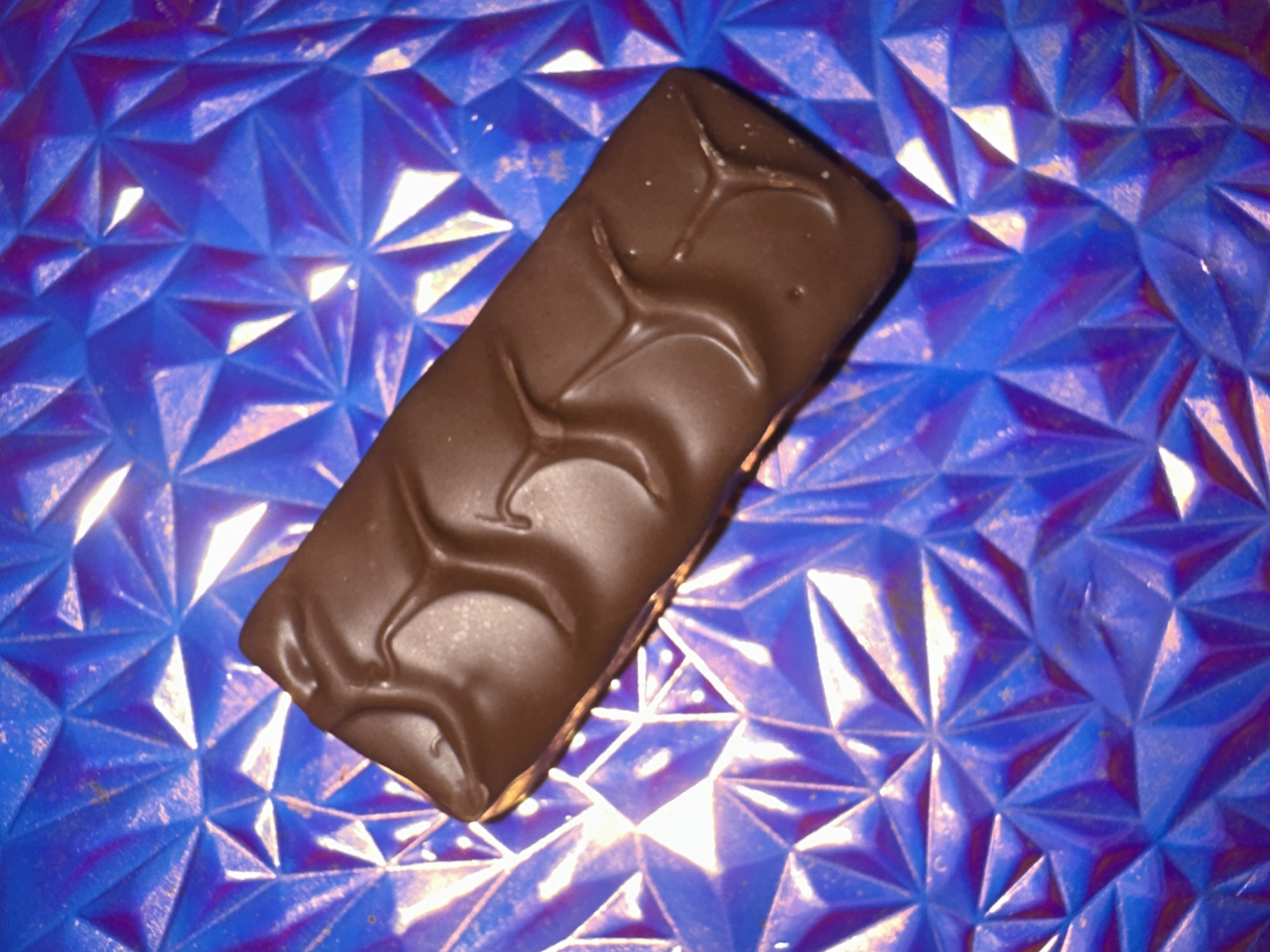 The image shows a chocolate bar resting on a geometric patterned surface that is blue. There are no people visible in the image, nor information about the location in Moscow, Russia.