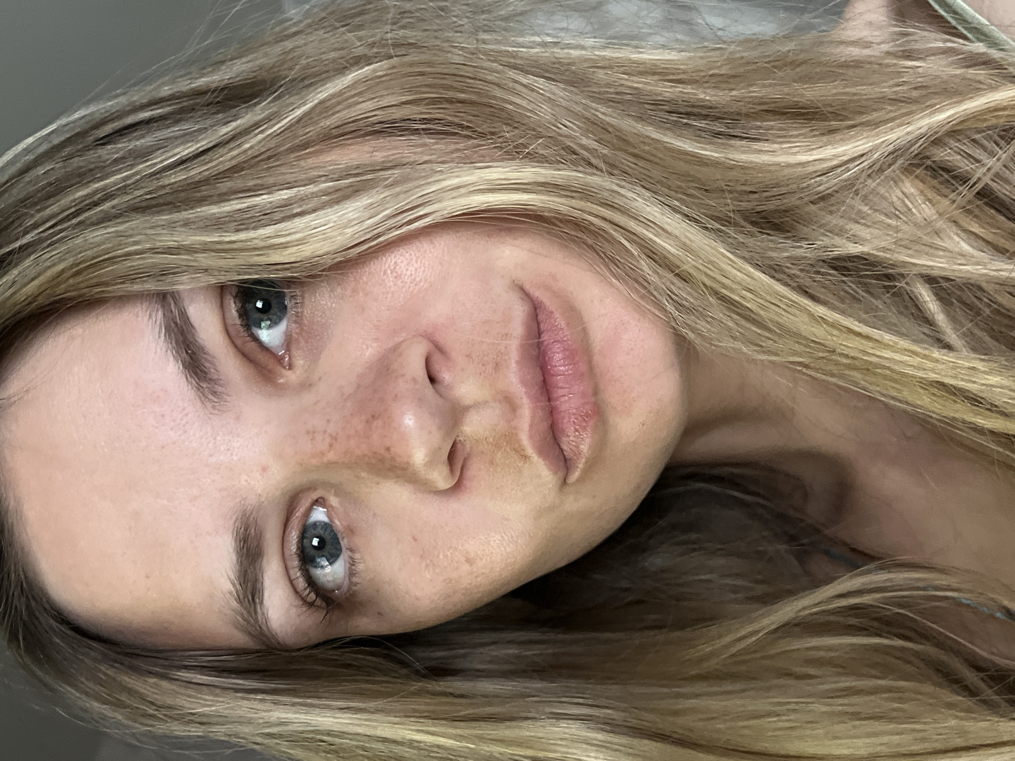 A close-up, slightly off-center, portrait-style image focuses on the face of a fair-skinned woman with light brown and blonde hair. Her eyes are light blue-gray. She has visible freckles on her nose and upper cheeks. The background is out of focus, appearing as a neutral gray-white. There is no indication that this image was taken in the city of Chaikovsky, Russia.