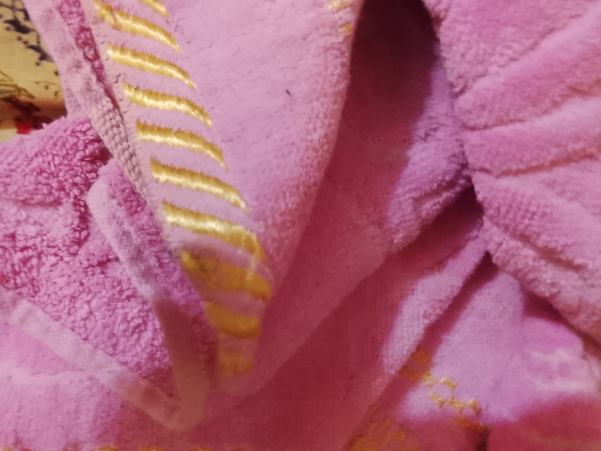 A close-up of a folded pink towel with gold stripes. Location: Cannot be determined from the image. No people or actions are discernible.