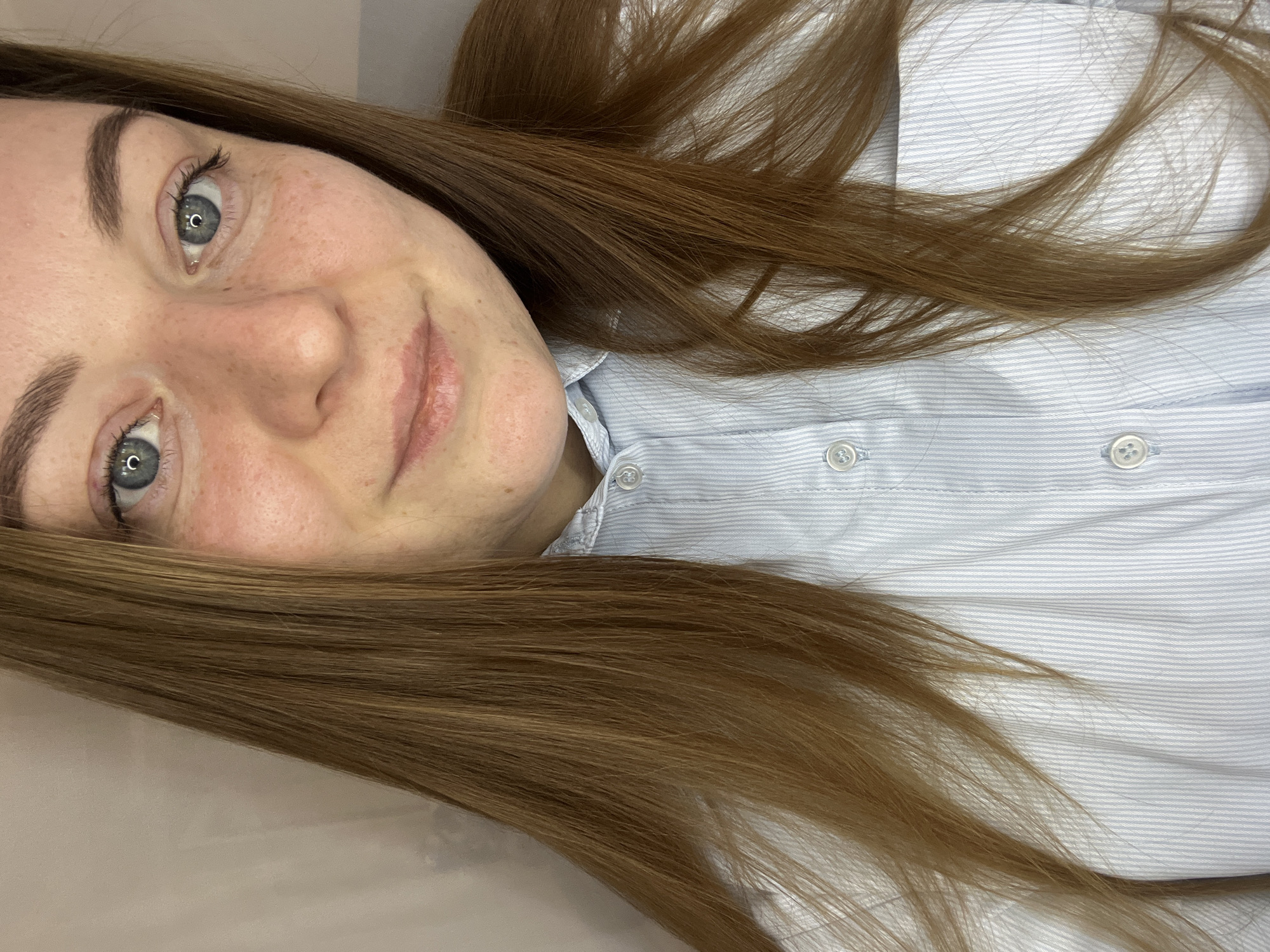 A close-up portrait of a woman with fair skin, light blue eyes, and freckles is shown. She has reddish-brown hair. She is wearing a light blue and white striped button-down shirt. The image appears to be taken indoors. There is no indication of the location being Раздолье, Russia.