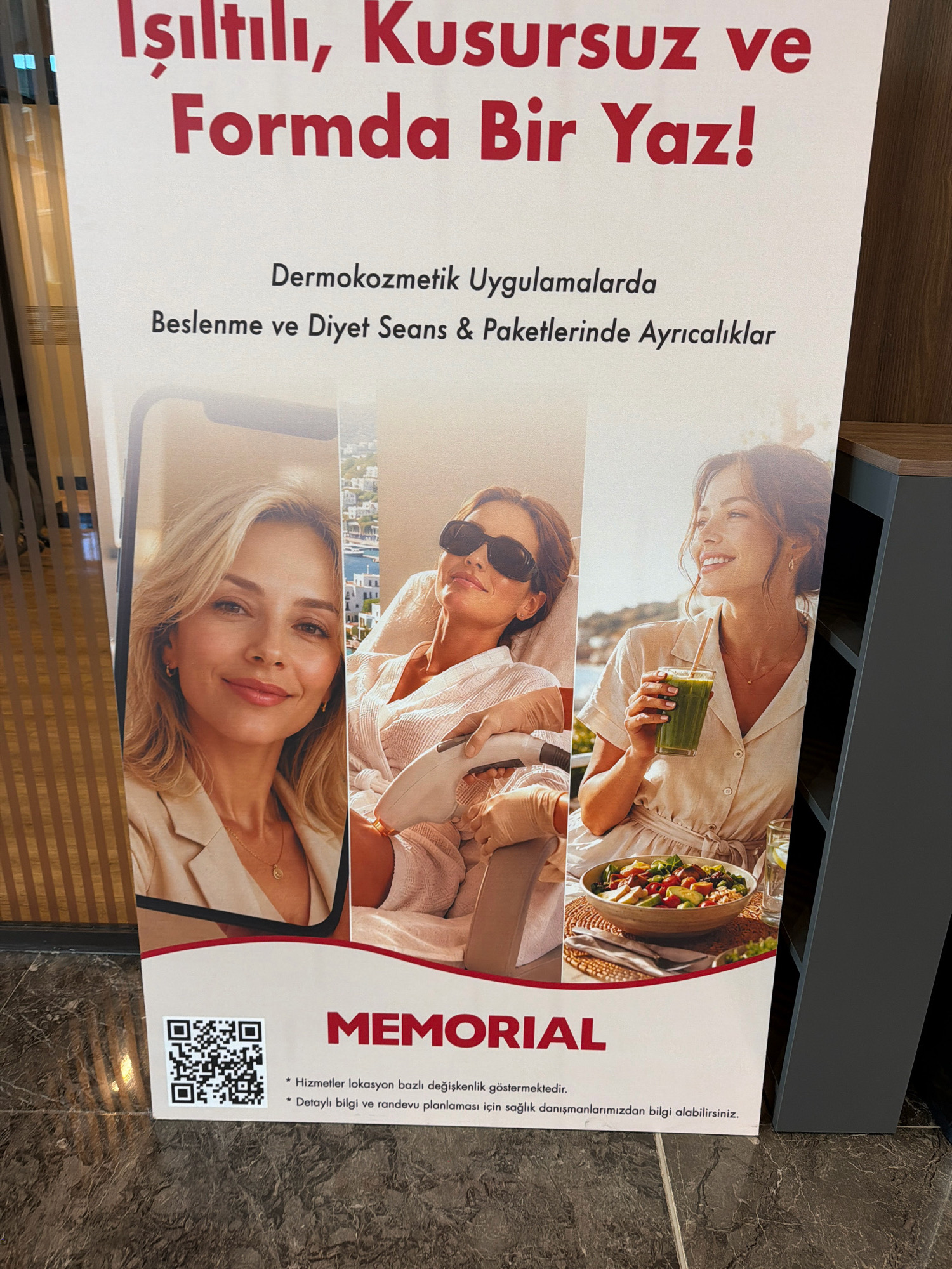 A vertical, close-up, full-frame photograph showcases a poster promoting wellness and beauty services at Memorial Ataşehir Hospital in Turkey. The poster features a slogan in Turkish, "Işıltılı, Kusursuz ve Formda Bir Yaz!" which translates to "A Shiny, Flawless, and Fit Summer!". Below the slogan, smaller text reads "Dermokozmetik Uygulamalarda Beslenme ve Diyet Seans & Paketlerinde Ayrıcalıklar," meaning "Privileges in Dermocosmetic Applications, Nutrition and Diet Sessions & Packages."
The main visual area of the poster is divided into three vertical panels. The left panel shows a close-up of a woman's face, with blonde hair and a gentle smile. She is wearing a light-colored blazer and a delicate necklace. The middle panel depicts a woman lying down, wearing a white robe and black sunglasses, with gloved hands operating a laser hair removal device. Behind her, a scenic view of white buildings and the sea suggests a resort-like setting. The right panel features a smiling woman in a light-colored dress, holding a green smoothie and looking off to the side. In the foreground of this panel is a bowl of salad.
At the bottom of the poster, a QR code is prominently displayed on the left. To its right is the "MEMORIAL" logo in large red letters, followed by two bullet points in Turkish, one stating that services may vary by location and the other advising to obtain information from health consultants for detailed information and appointment planning. The poster is mounted on a textured wall, and the lower part of the image shows a dark, marbled floor. The lighting is bright, suggesting an indoor environment with good illumination.