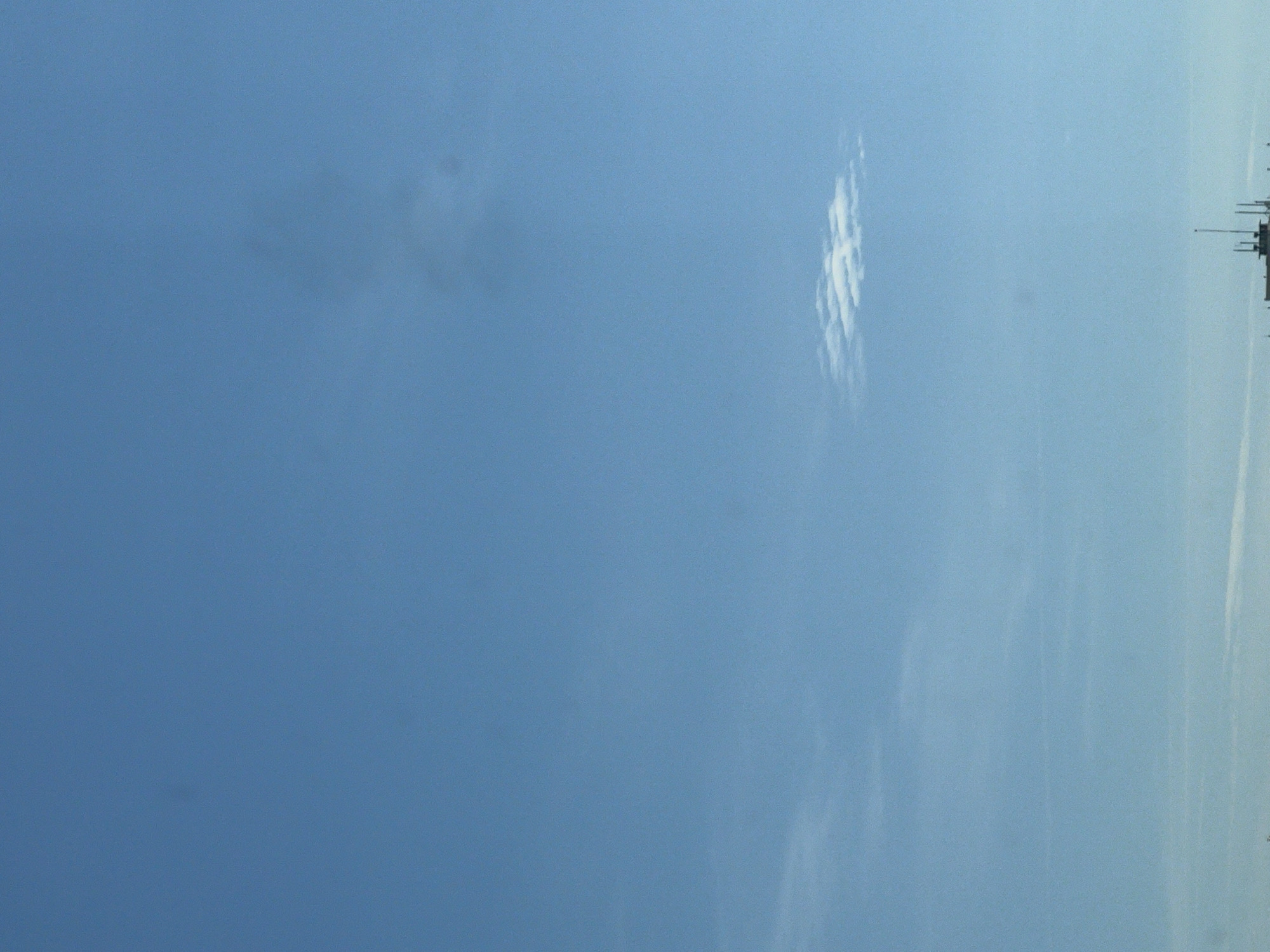 The image shows a bright blue sky with a few thin clouds. In the lower part of the image, there is a building with several antennas. This building appears to be a communication tower or a similar structure. The sky is clear and the sun appears to be shining, creating a bright and airy atmosphere. The image does not contain any people. The location is identified as Warsaw, Poland.
