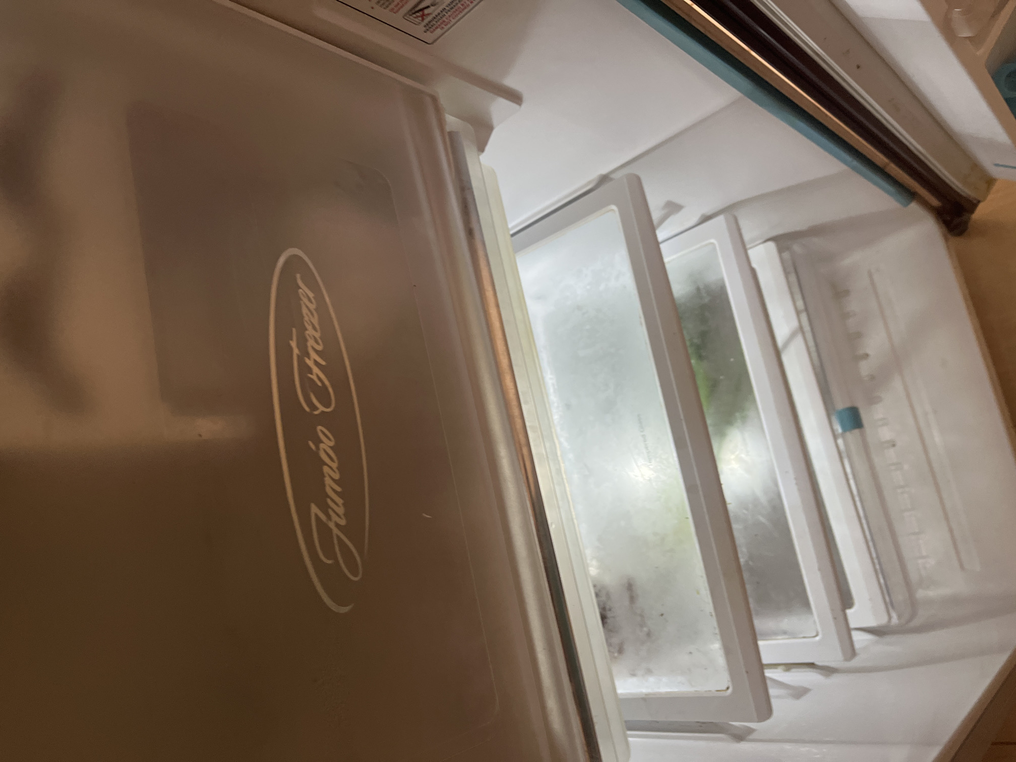The image shows the interior of an open refrigerator or freezer. The lid of the appliance is open, revealing shelves and drawers within. The branding "Jumbo Freezer" is visible on the inside of the lid in an oval shape. The shelves appear to be made of glass or clear plastic, and there is some condensation or frost present on them. The overall environment appears to be a domestic kitchen. The location of Cirahayu, Indonesia is not depicted or suggested in the image.