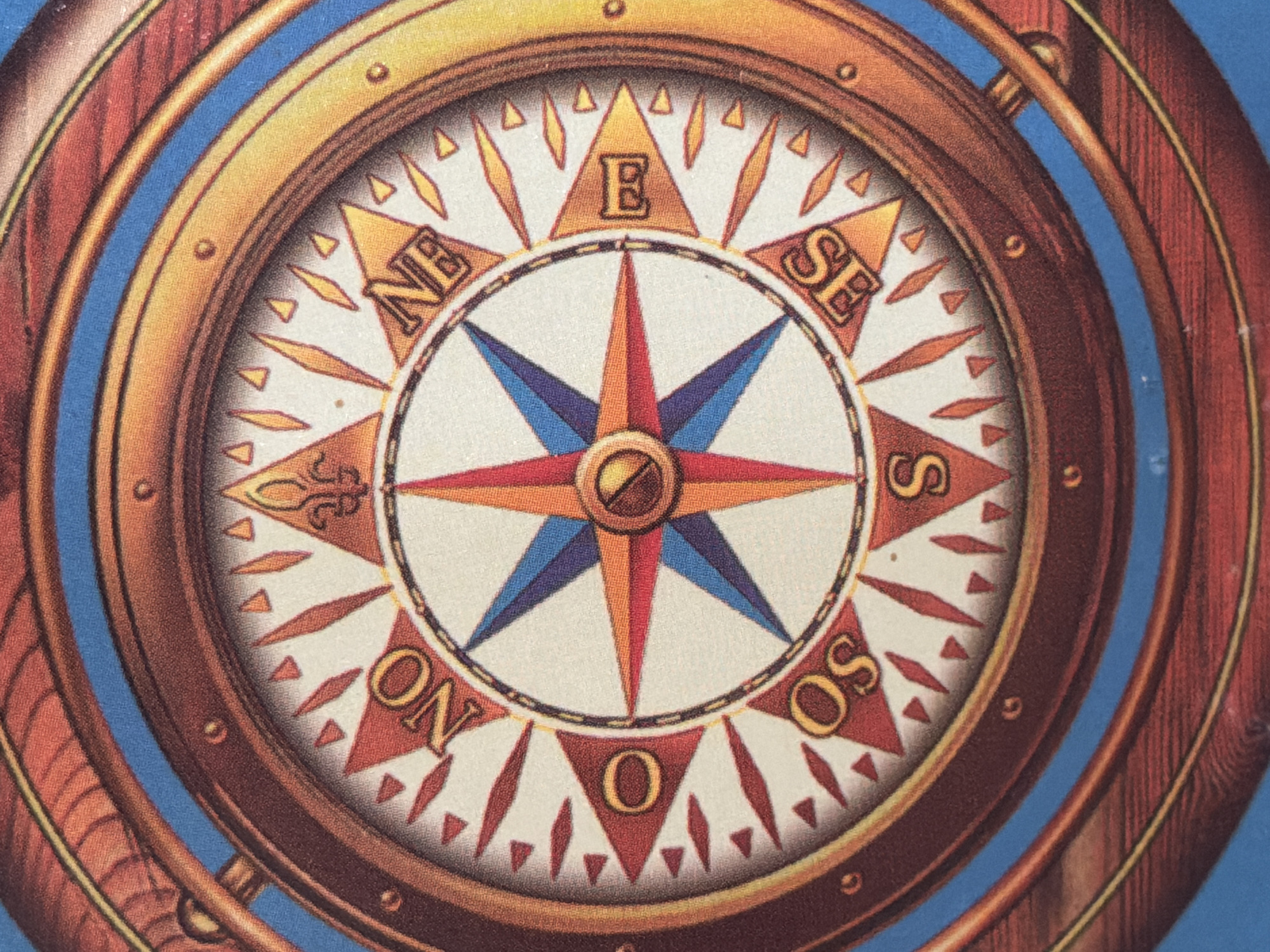 The image displays a close-up, overhead view of a decorative compass, likely a printed illustration or part of a nautical-themed object. The compass features a detailed design with a prominent star-shaped needle in red, blue, and orange. Around the center, cardinal directions are marked with stylized letters on a white background, including "NO" for North, "NE" for Northeast, "E" for East, "SE" for Southeast, "S" for South, "OS" (likely West), and parts of other directional indicators. The compass is surrounded by a textured, wooden-rimmed frame with metallic accents and appears to be set against a blue background. There are no people, animals, or any indication of a specific city or location like Arcahueja, Spain.