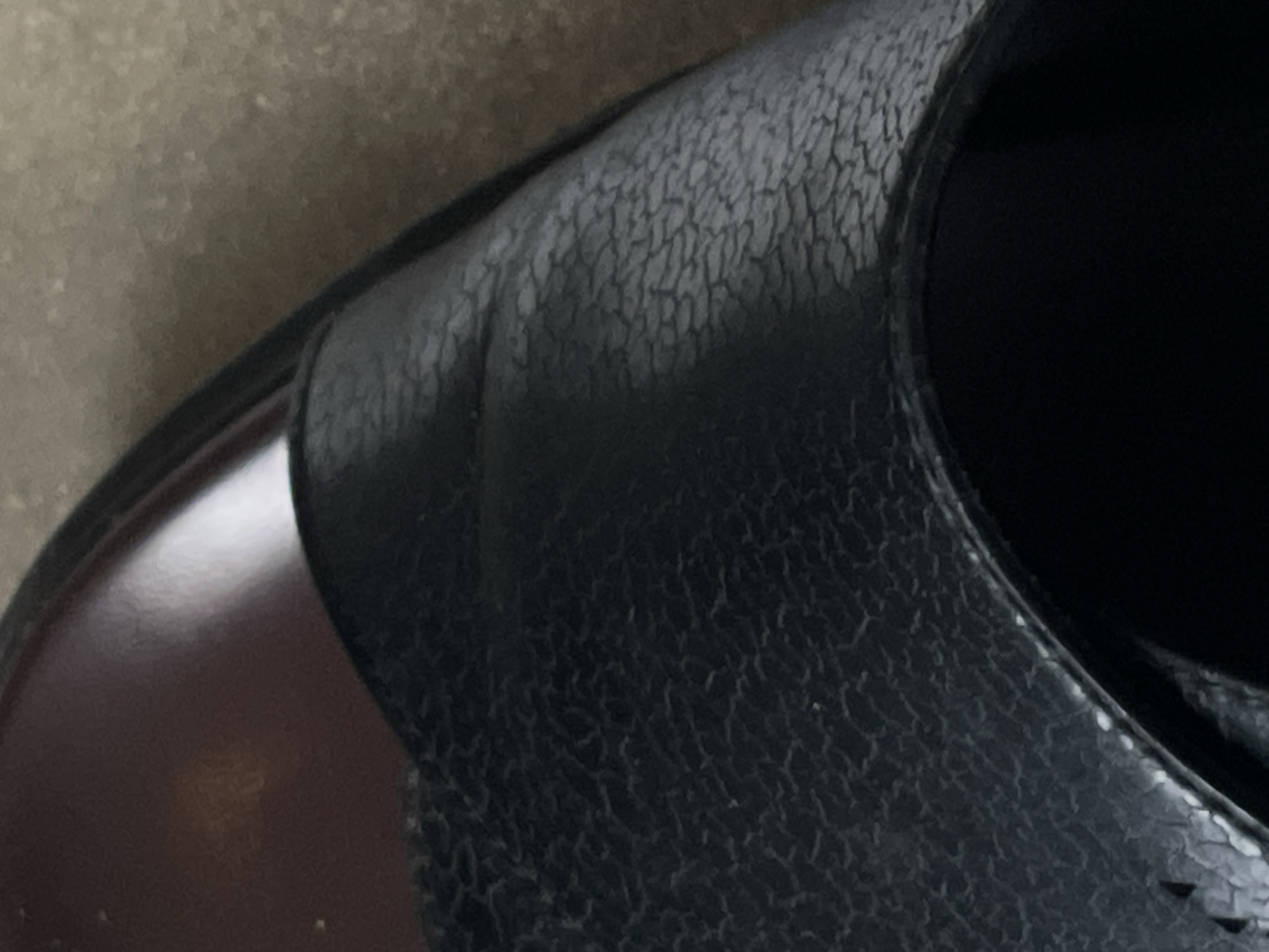 Close-up of a leather shoe with black textured leather trim. Part of the shoe is a highly polished brown. The background is a textured tan color.