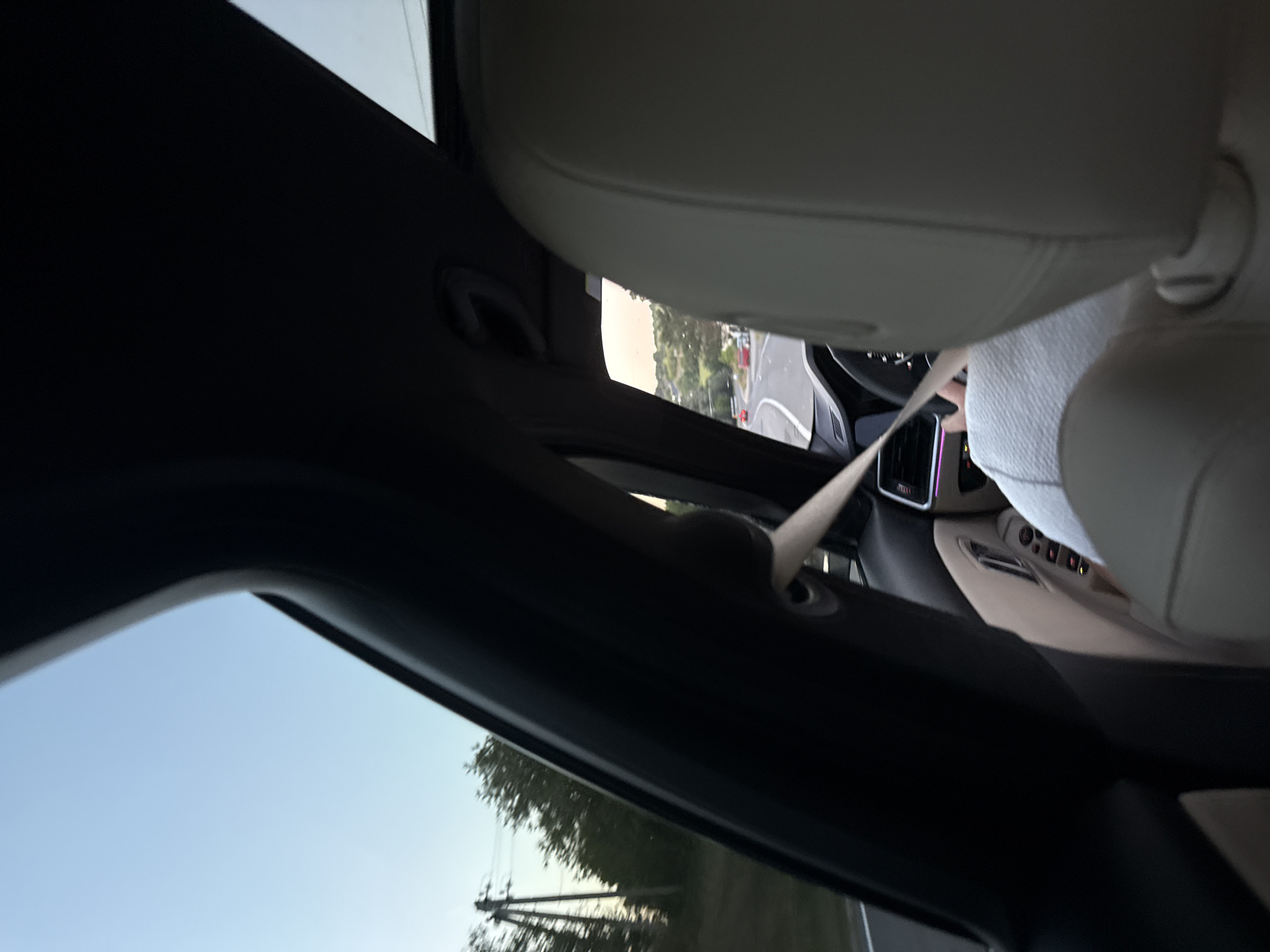 The image shows the interior of a car, likely in motion, with a view through the passenger side window. A light-colored seat and a beige leather interior are visible. A seatbelt is extended across the frame. Outside the window, a road is visible with some trees and utility poles. The sky is clear and blue. The general lighting suggests it is daytime. The image is taken from inside the car, looking towards the front and side. The location of Fundul Galbenei, Moldova is not discernible from the visual information present in the image.