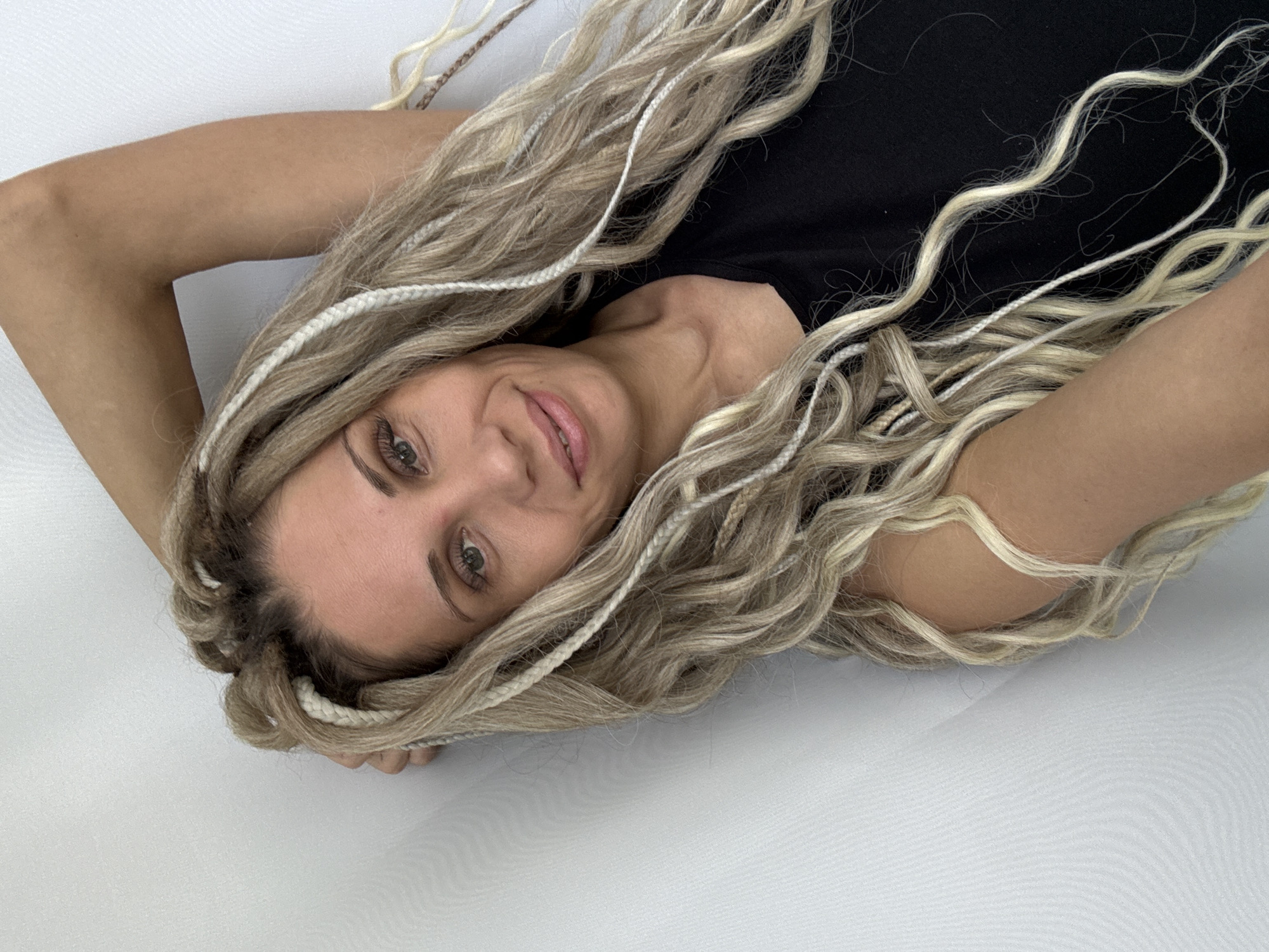 The image shows a woman with light blonde hair in a braid style, lying on a white surface. She is wearing a black top. The location is unknown, and there is no evidence to suggest it is in Rusanovo, Russia.