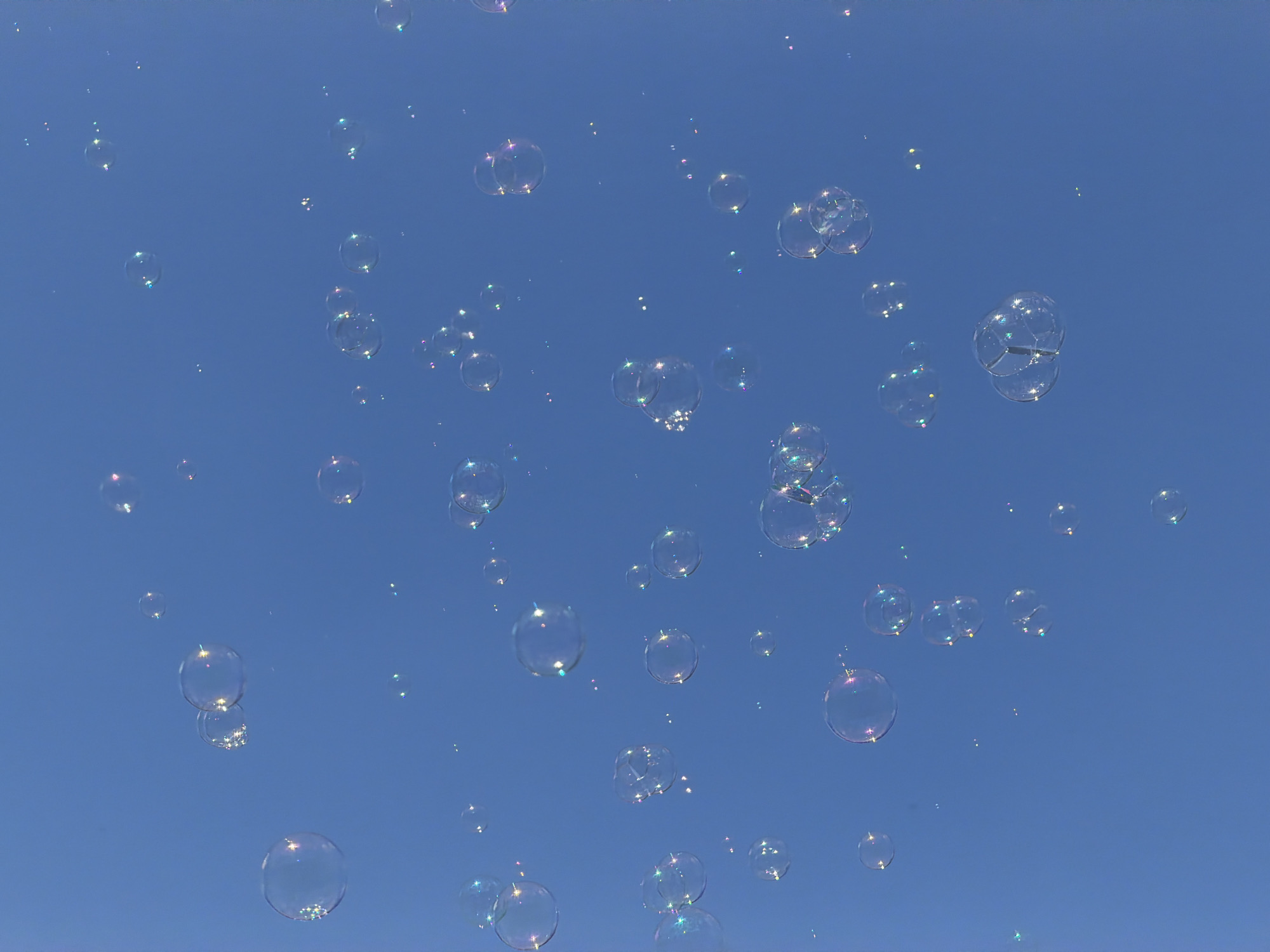 The image shows numerous soap bubbles floating in a clear blue sky. There are no people visible. The location is not discernible from the image; there is no information to suggest it is in Sofia, Bulgaria.